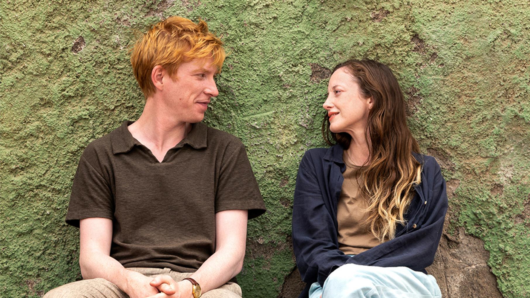 Jack and Alice sit and look at each other in front of a greenish wall