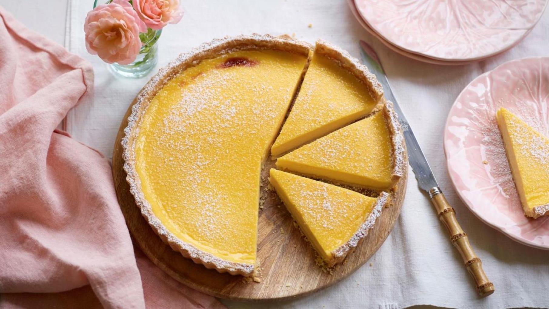 A passion fruit tart partially cut into slices on a table with cloths, plates, and flowers