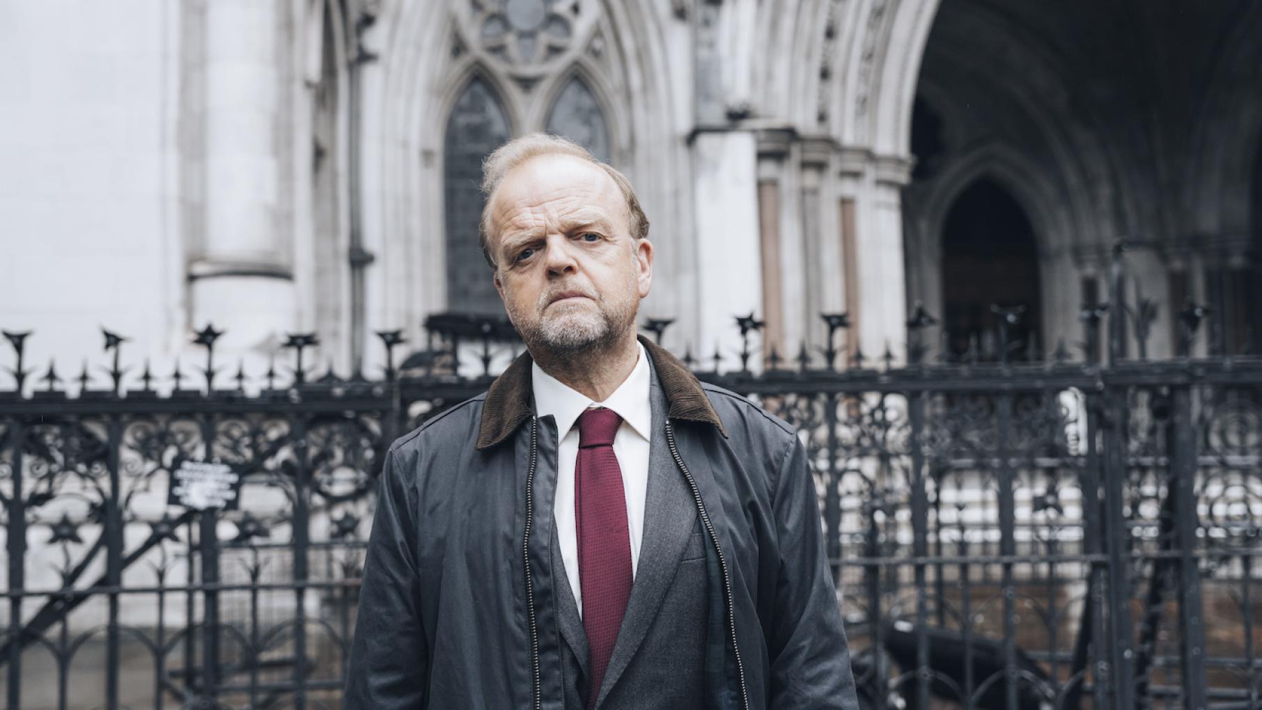 Mr Bates stands looking serious in front of a fence