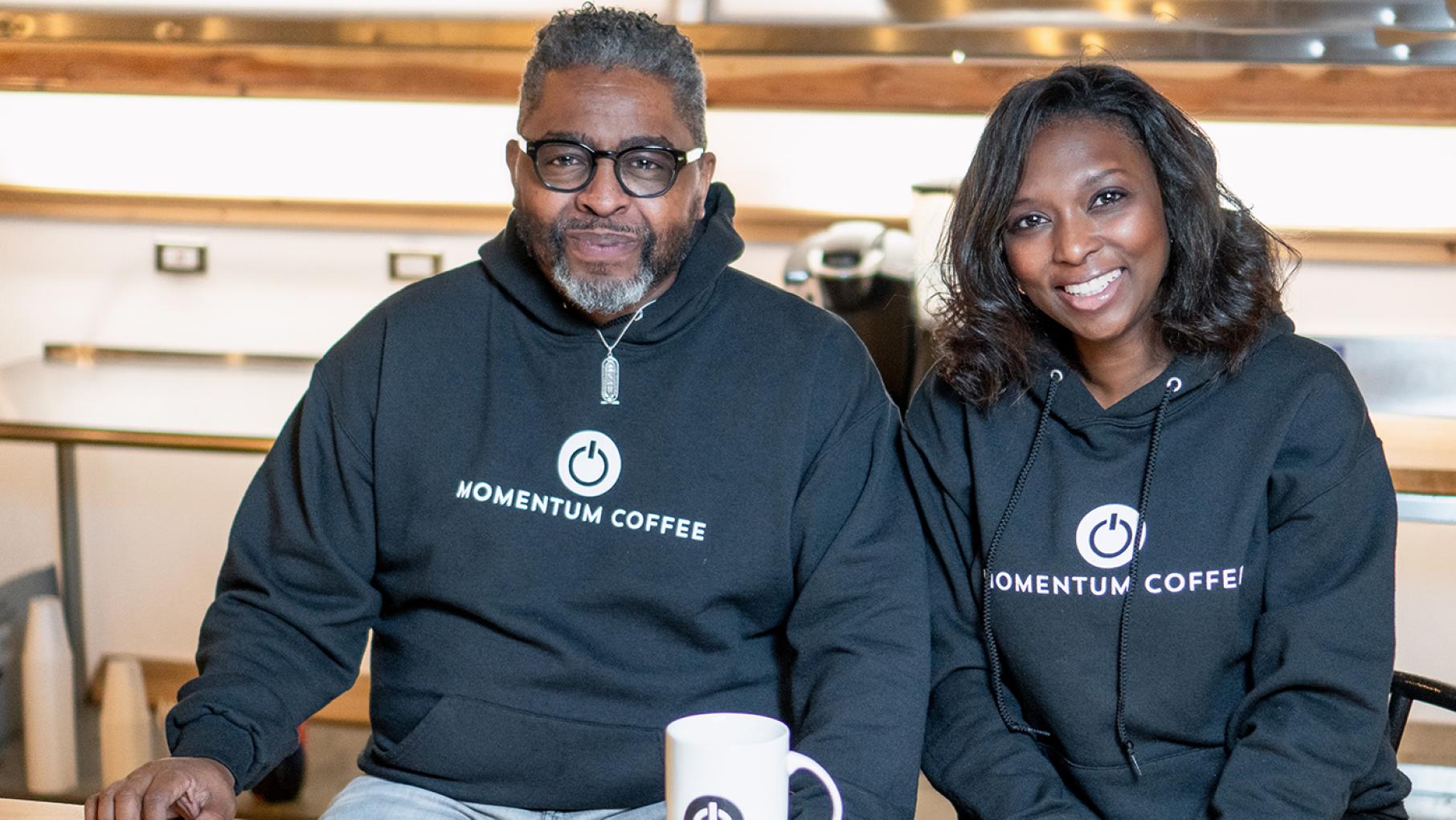 “We want to be a catalyst for development in these neighborhoods that have been abandoned for over 60 years now,” says Momentum Coffee's Tracy Powell, pictured here with Nikki Bravo. Credit: Momentum Coffee Tracy Powell and Nikki Bravo pose for a photo in sweatshirts branded Momentum Coffee