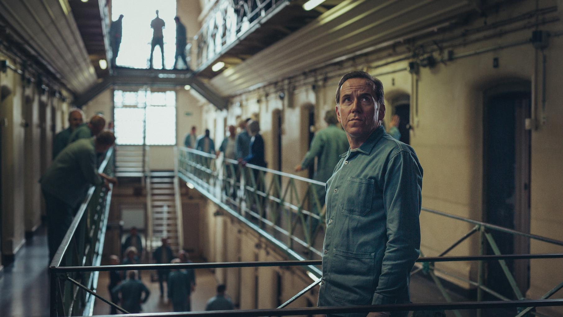 Professor T looks up while standing on a bridge in a prison
