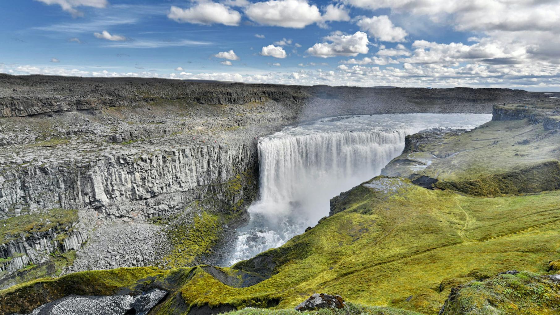 A waterfall in a rocky and grassy landscape against a blue sky