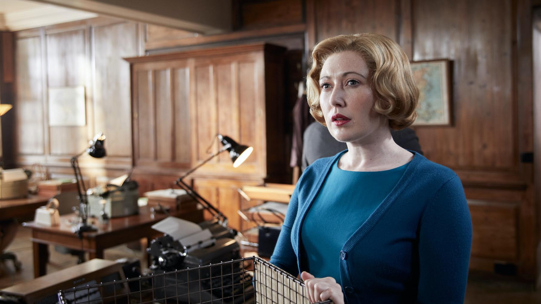 Miss Scott looks intently offscreen in a wood-panelled room