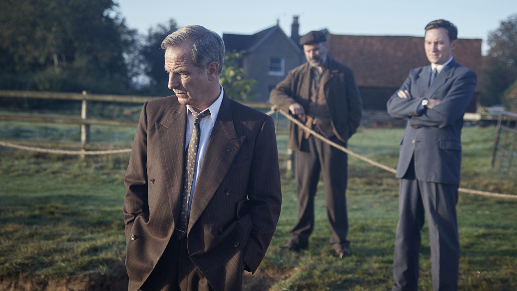 Geordie looks down at the ground in a field in front of Larry and a farmer