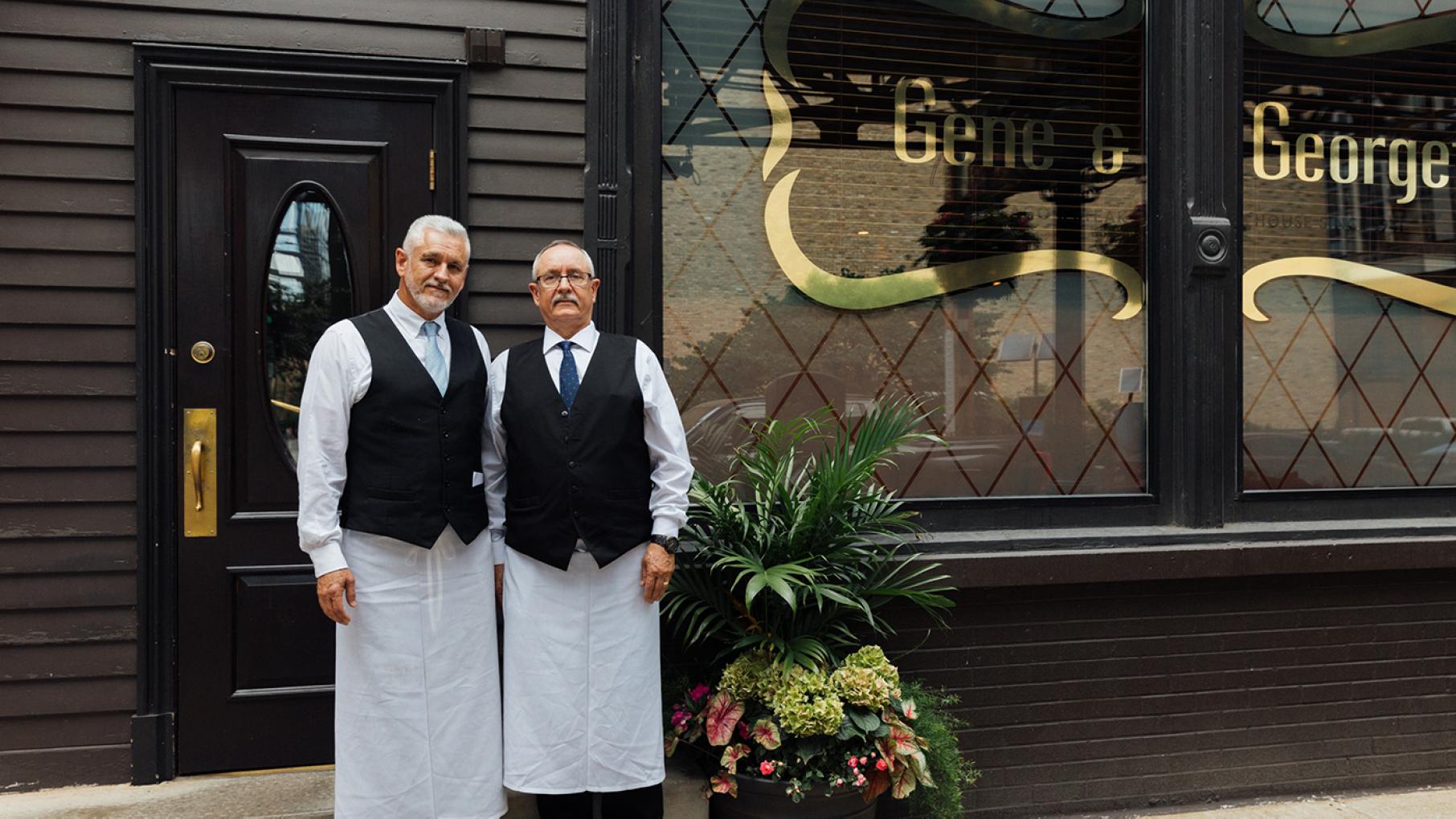 J.J. (left) and Juan (right) Muñoz have worked at Gene & Georgetti for a combined 72 years. Credit: Sandy Noto for WTTW The Muñozbrothers stand in their uniforms outside the door of Gene & Georgetti