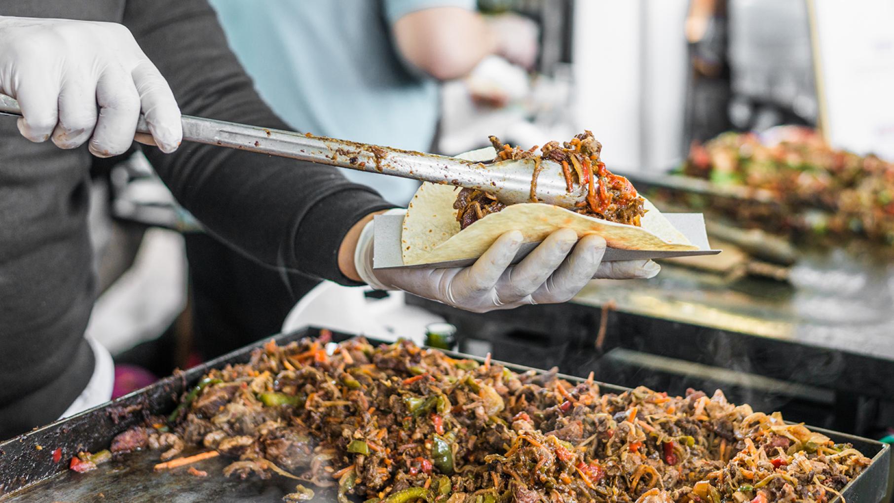 A person filling a taco with tongs