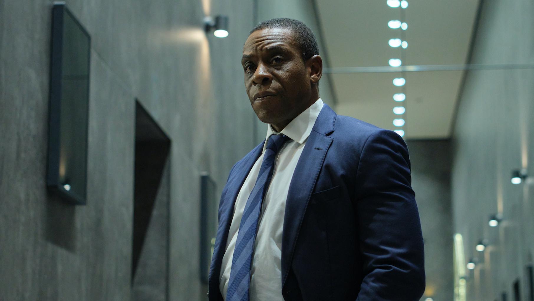 Joseph feels that Robert is using him as a scapegoat for criticism of the government's police approach. Credit: Sky Studios Limited Joseph Obasi stands in a suit and looks stern