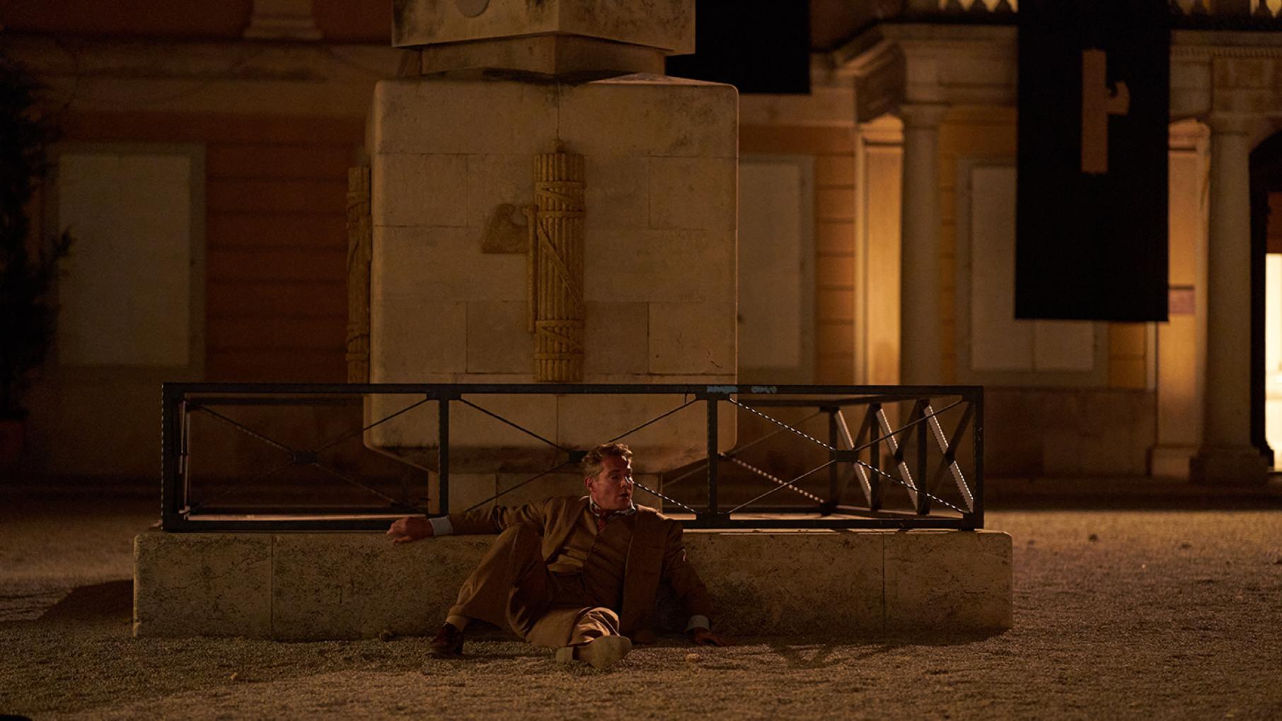 Cecil sprawls on the ground in front of a fountain at night