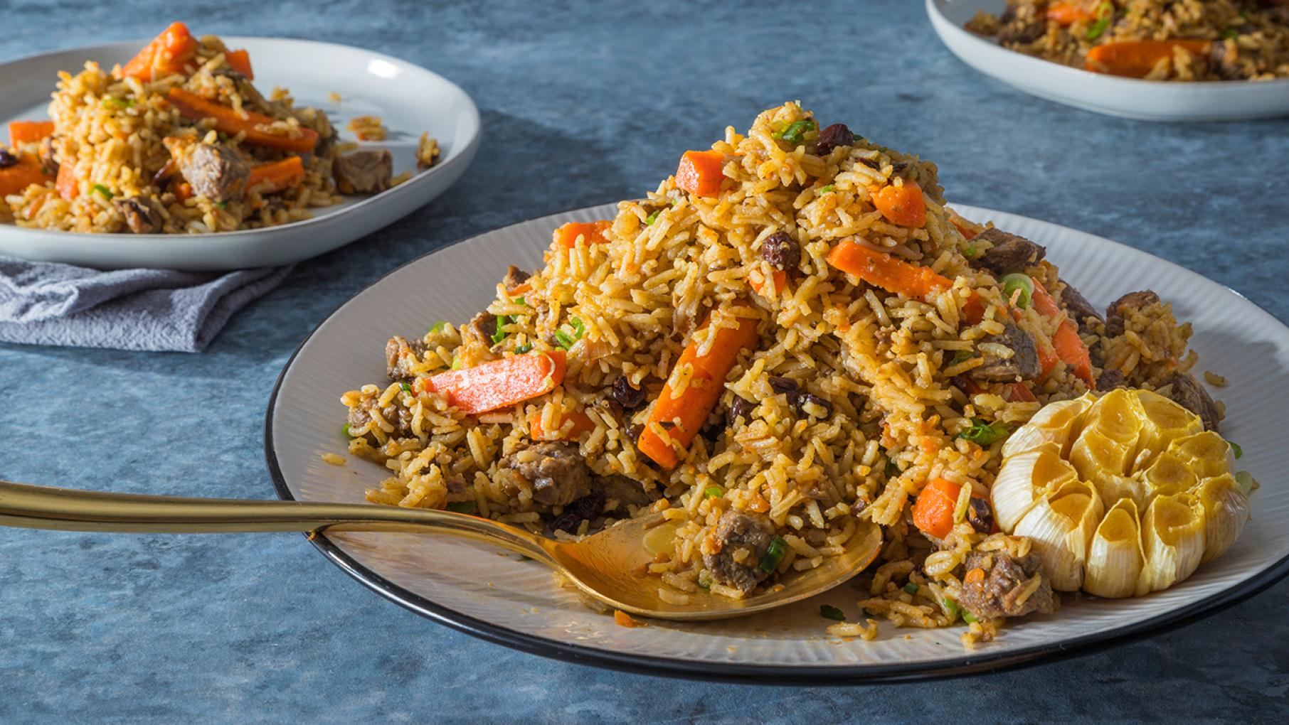 Plates heaped with rice, beef, and vegetables on a blue table