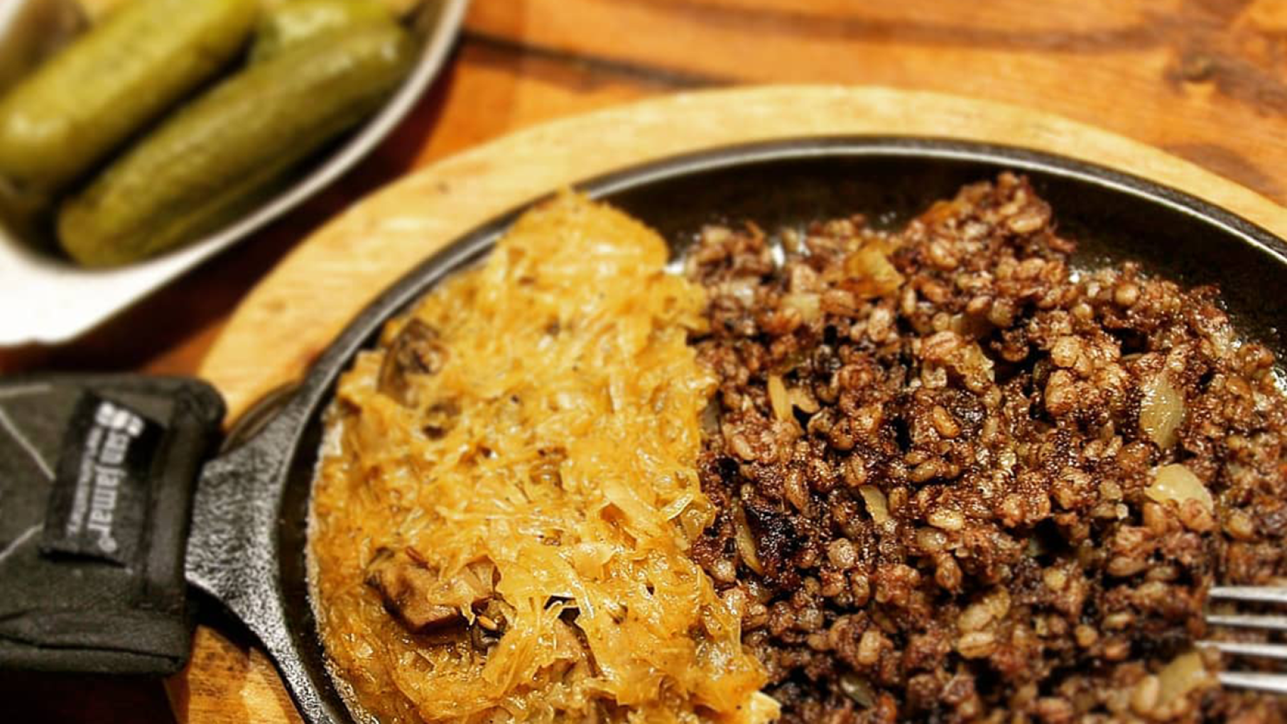 A skillet of cooked sauerkraut and kishka with pickles in the background