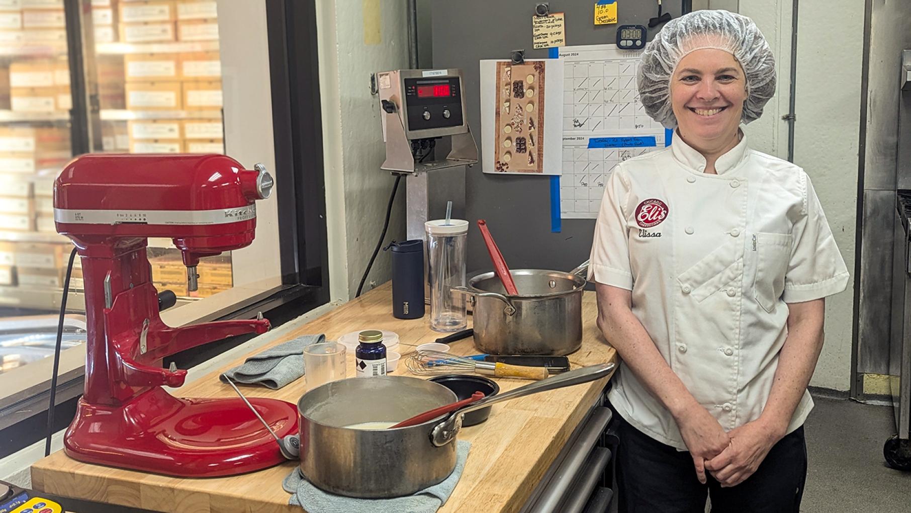 Elissa Narow works in the innovation department at Eli's Cheesecake. Credit: Lisa Futterman for WTTW. Elissa Narow standing at a work station with a large mixer