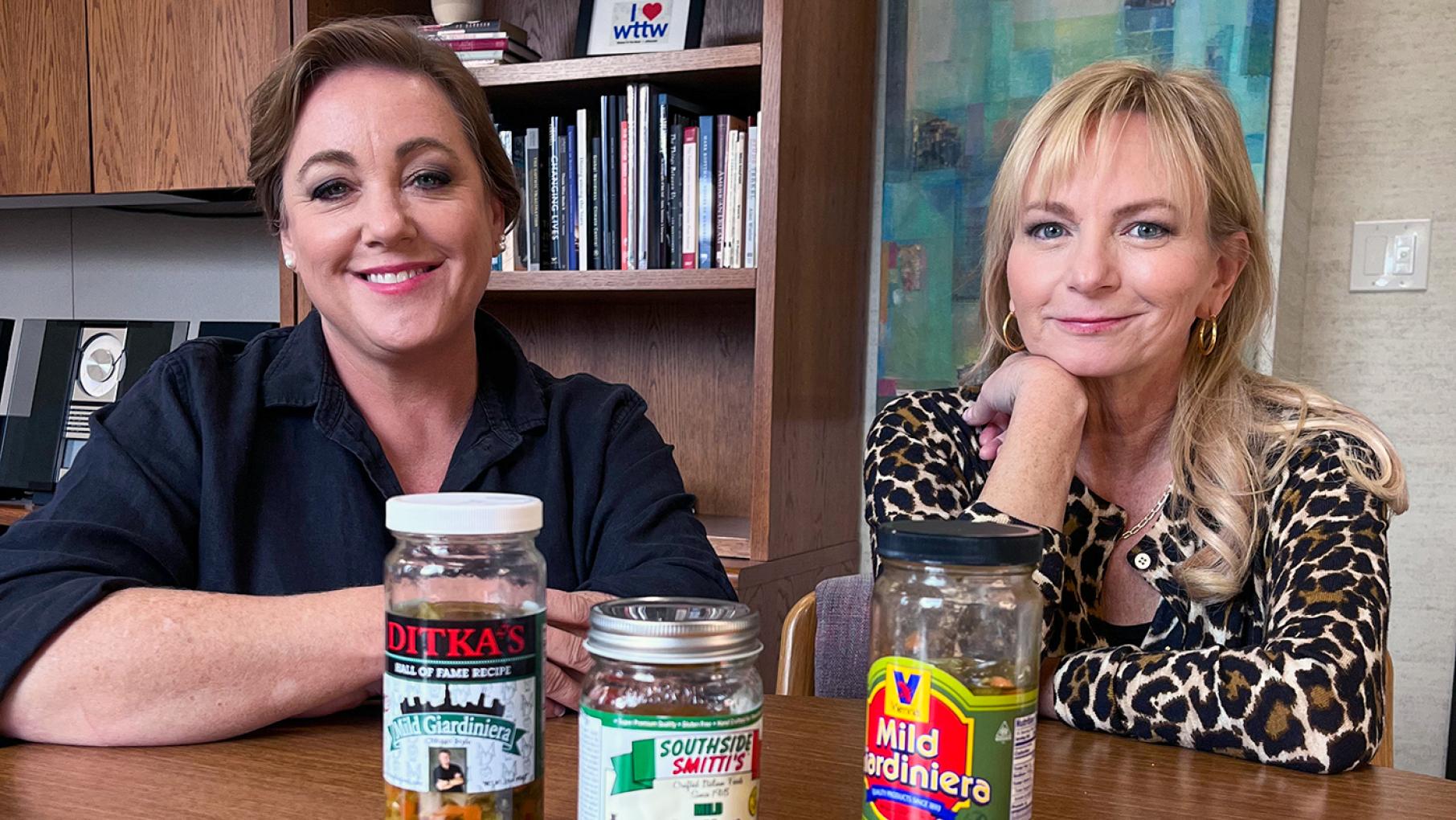 Two hosts of America's Test Kitchen sit at a table and smile behind three jars of giardiniera