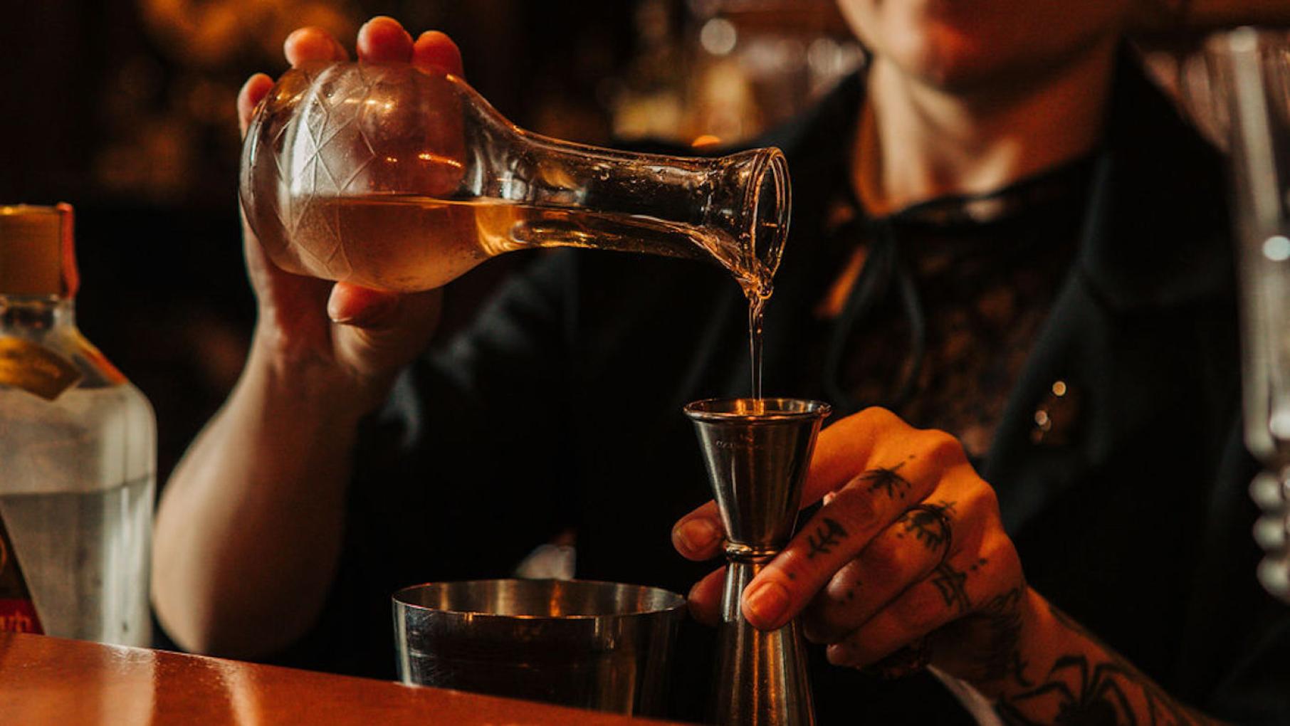 Milk Room manager Sam Parrie adapted a cocktail recipe from a 1927 book by a legendary bartender. Credit: Keni Rosales Hands pour a liquid into a jigger behind a bar