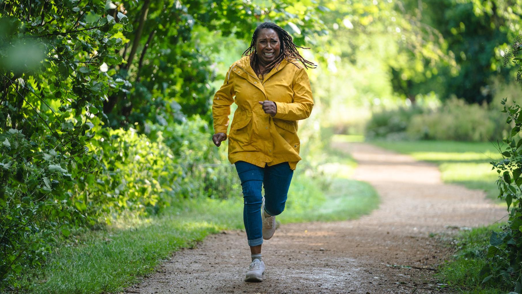 Suzie runs down a forested path in a yellow raincoat