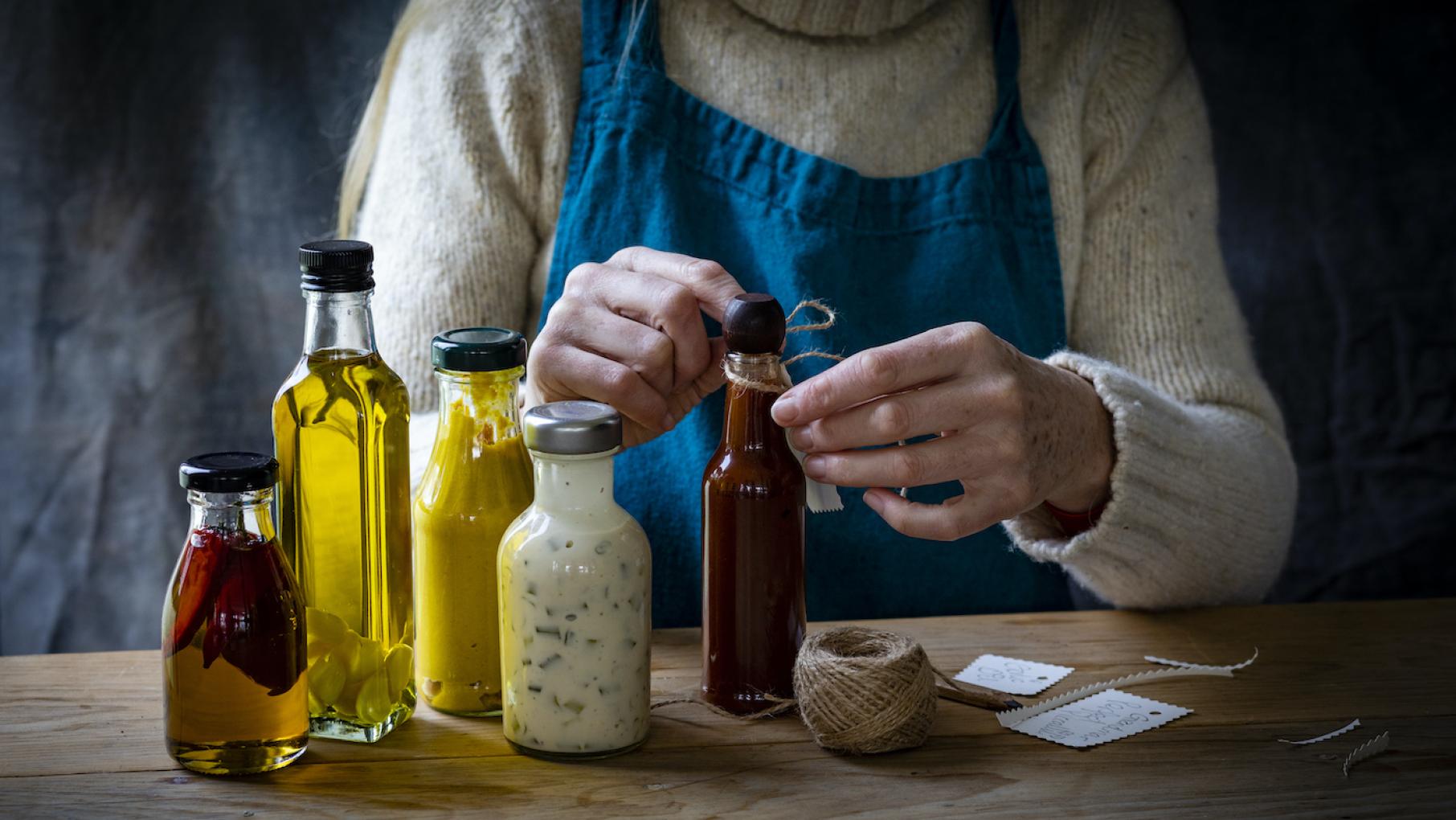 Credit: iStock A woman tying handmade name cards onto bottles of homemade oils and food dressings with twine