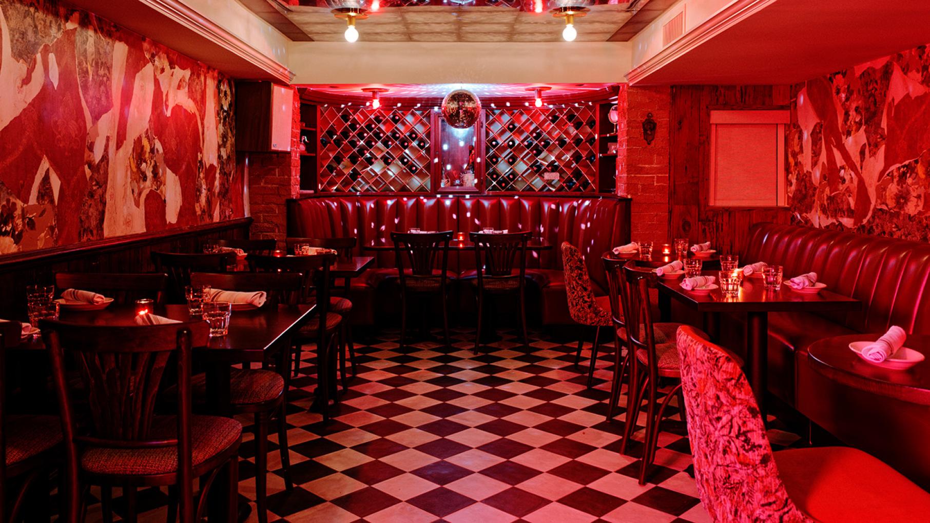 The transformation of the decades-old La Cantina in the basement of Italian Village into Sotto involved keeping many of the details along with some contemporary updates. Credit: Jack X. Li The red-lit interior of a restaurant with red banquettes and a disco ball