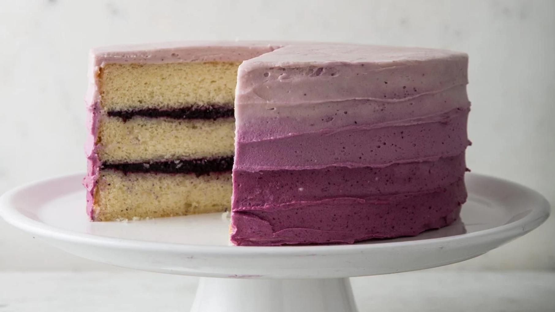 Credit: Joe Keller for 'Cook's Country' A cake on a cake stand with a slice taken out revealing layers of blueberry jam, frosted on the outside in a purple ombre gradation