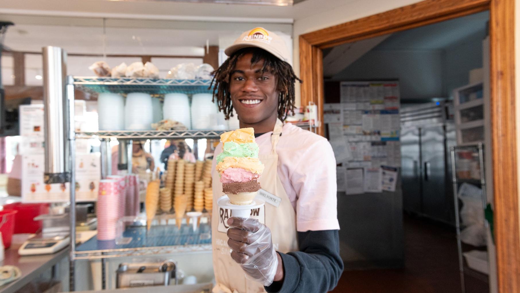 The Original Rainbow Cone employee Shelvonte Anthony holds the shop’s namesake treat, a cone with orange sherbet on top of pistachio, Palmer House, strawberry, and chocolate ice cream. Credit: Gonzalo Guzman for WTTW Employee Shelvonte Anthony holds a very large ice cream cone