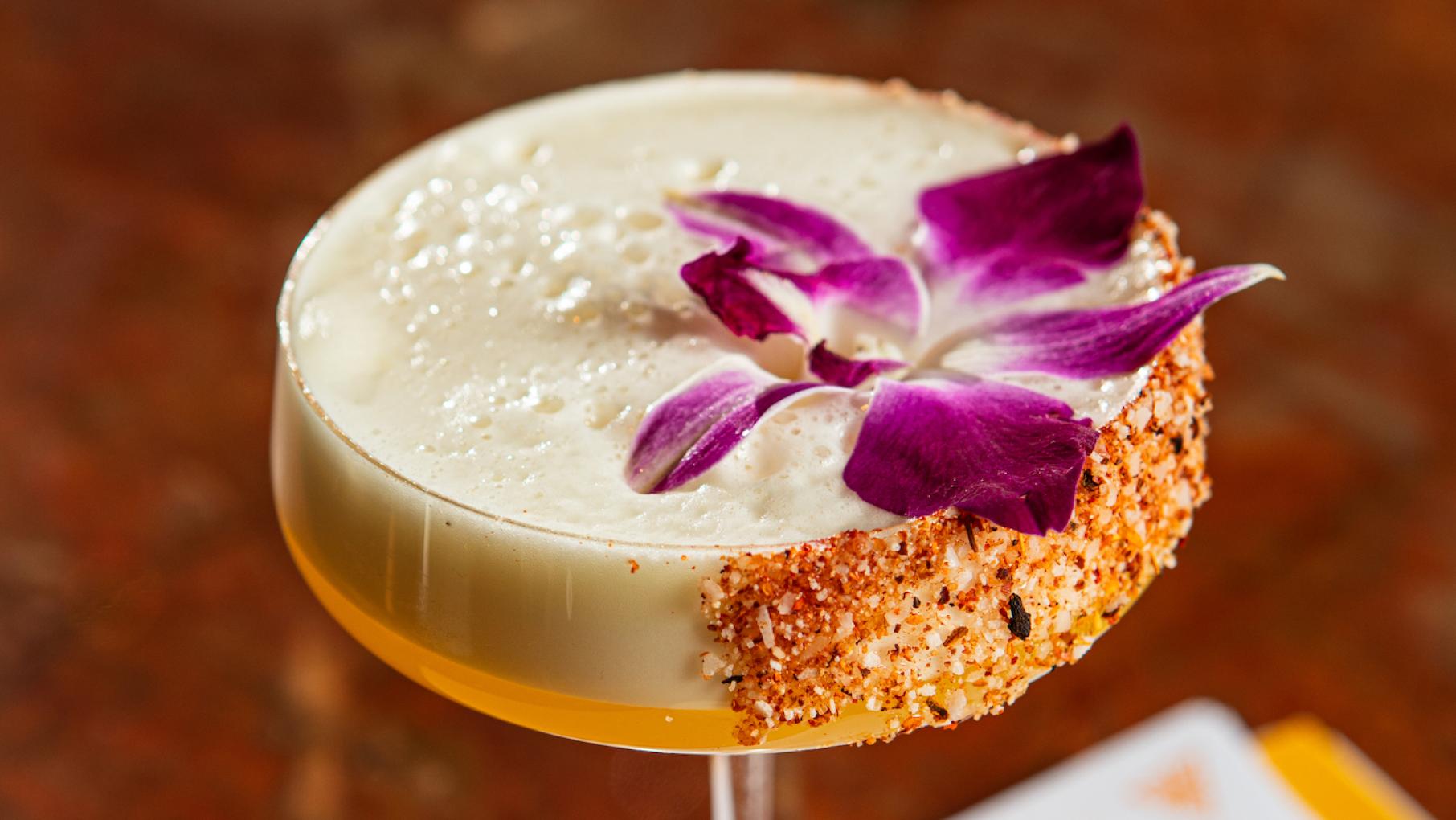 A creamy cocktail in a coupe class with a purple flower on top