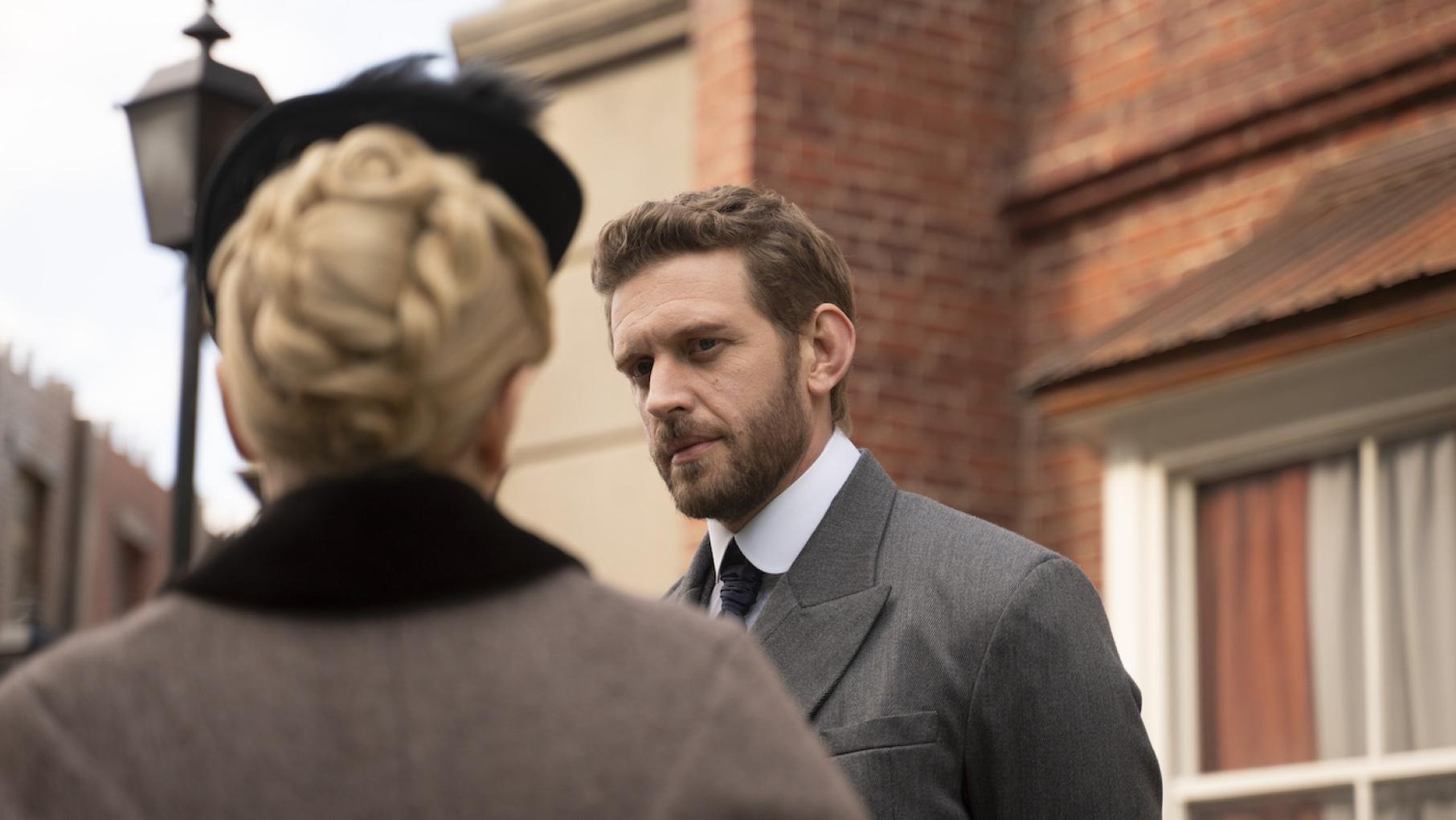 Alexander Blake looks at Miss Scarlet, who is facing away from the camera