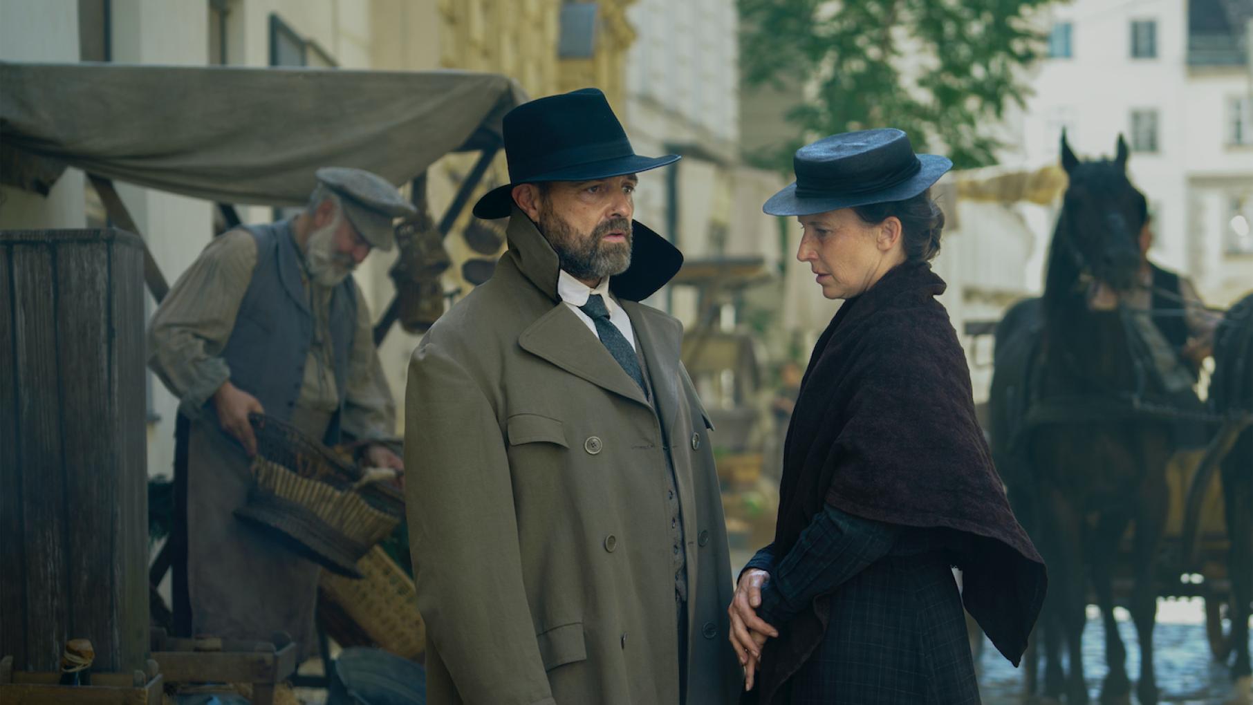 Oskar, with his collar turned up and a hat on, speaks to Therese in the street