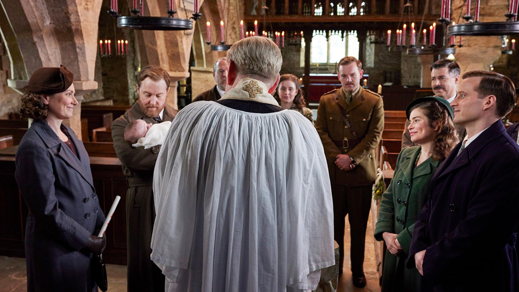 The whole family is reunited for Jimmy's christening. Credit: Helen Williams for Playground Entertainment and Masterpiece A priest stands with his back to the camera with others gathered around him