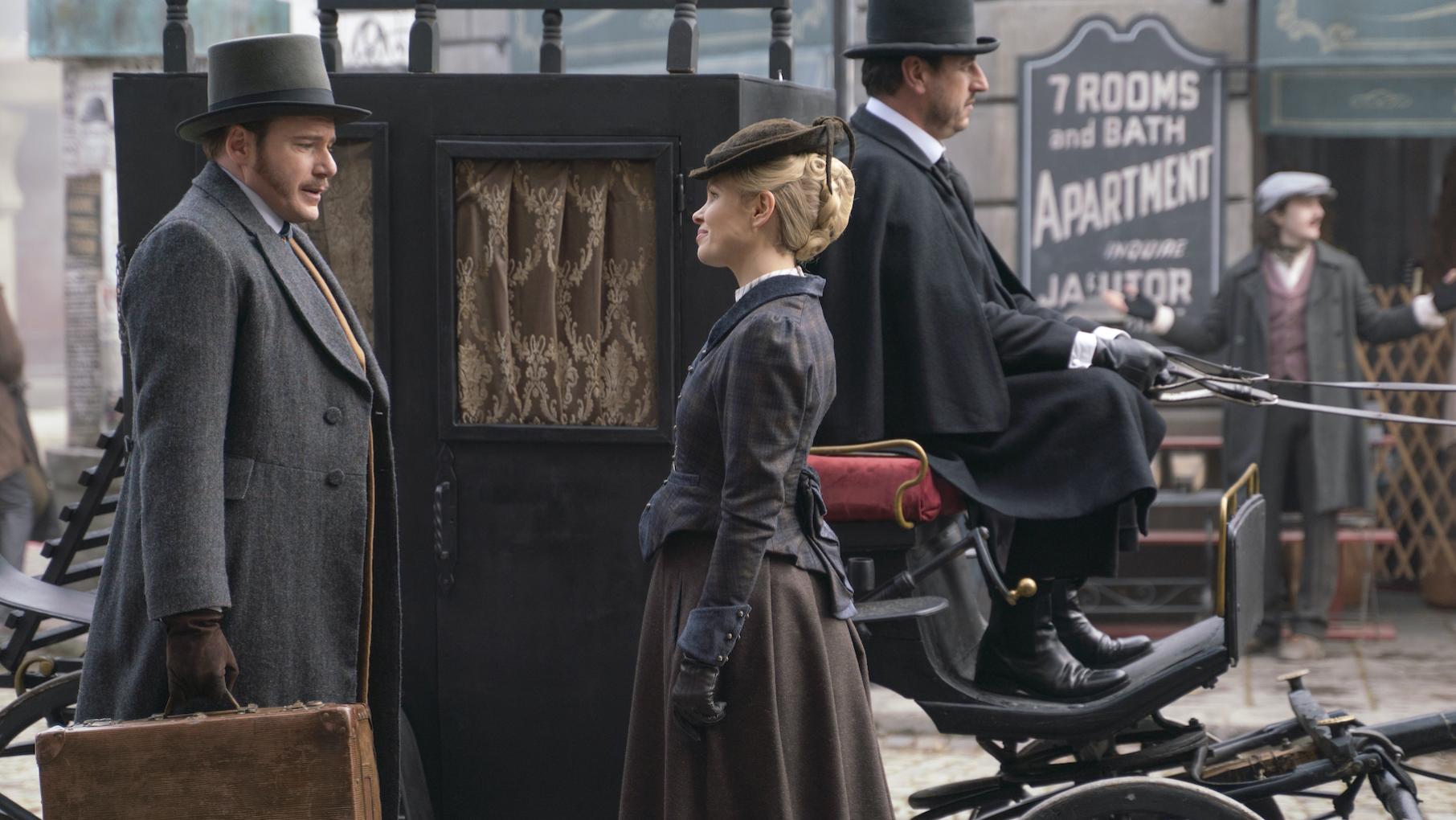 Nash holds a suitcase outside a carriage and faces Eliza