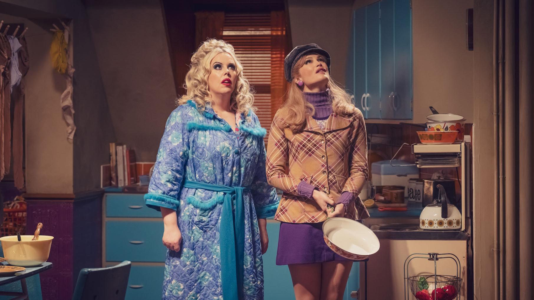 Greta and Sophie look up at the ceiling in a kitchen while Sophie holds a pan
