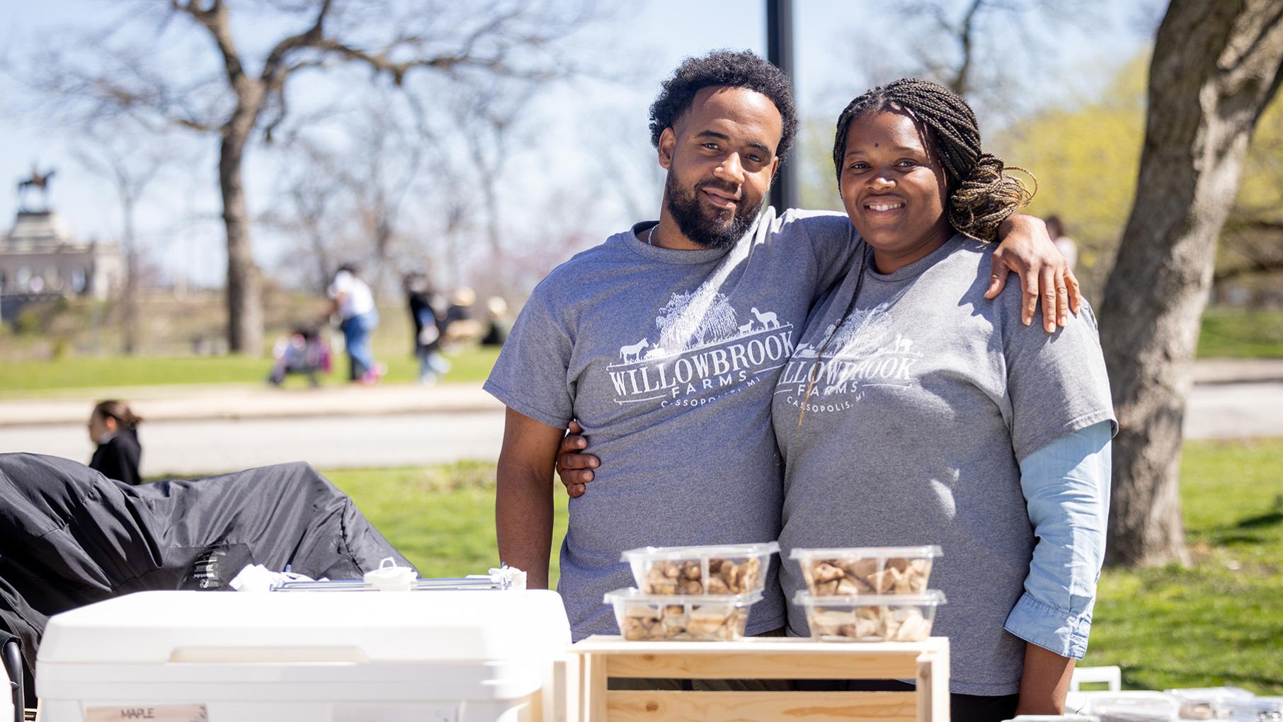 Juan and Vanessa Frias of Willowbrook Farms at Chicago's Green City Market in 2024. Credit: Kathleen Hinkel for WTTW The owners of Willowbrook Farms smile behind a table of their goods at a farmers market