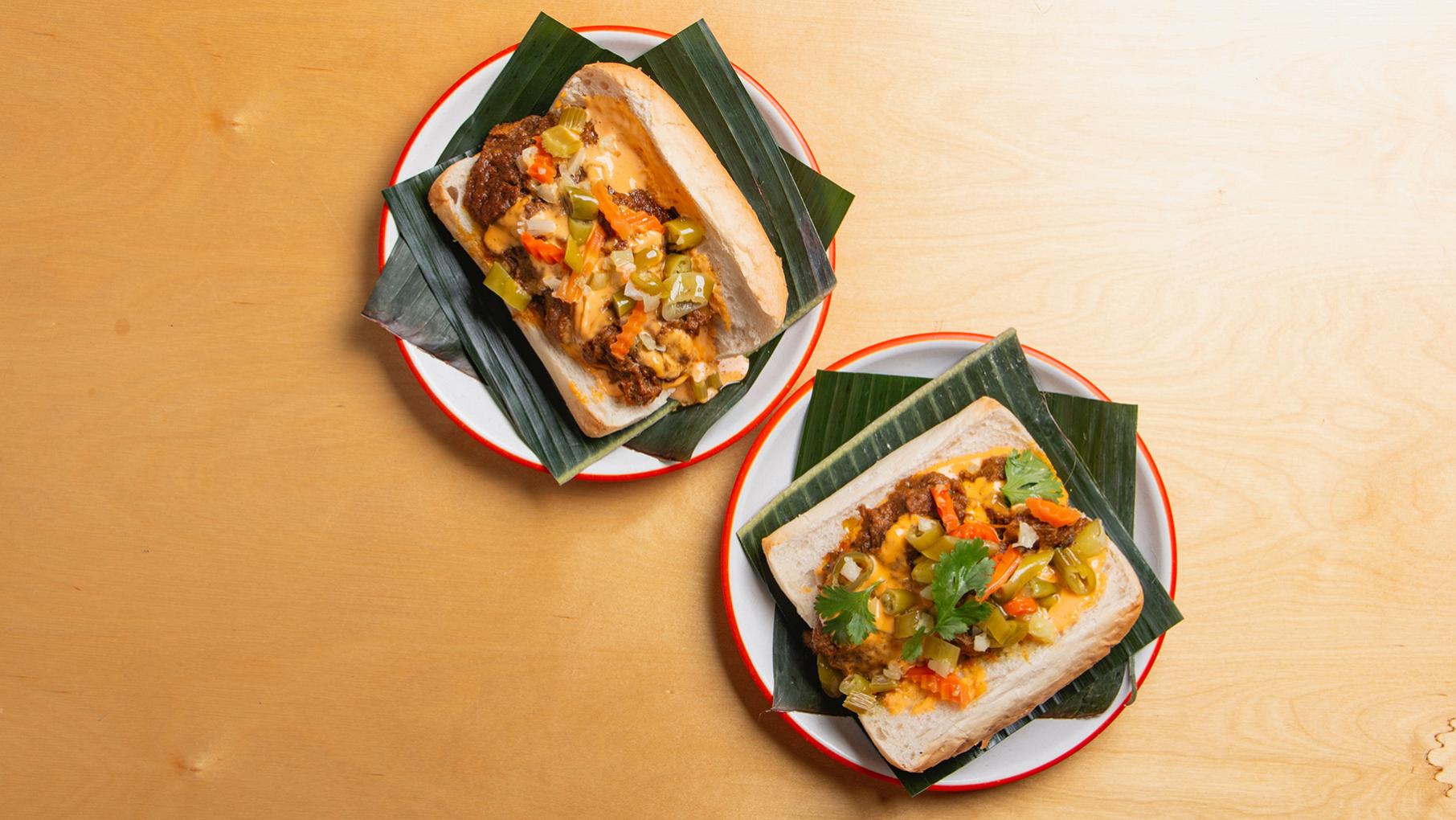 Two sandwiches on leaves on plates seen from above