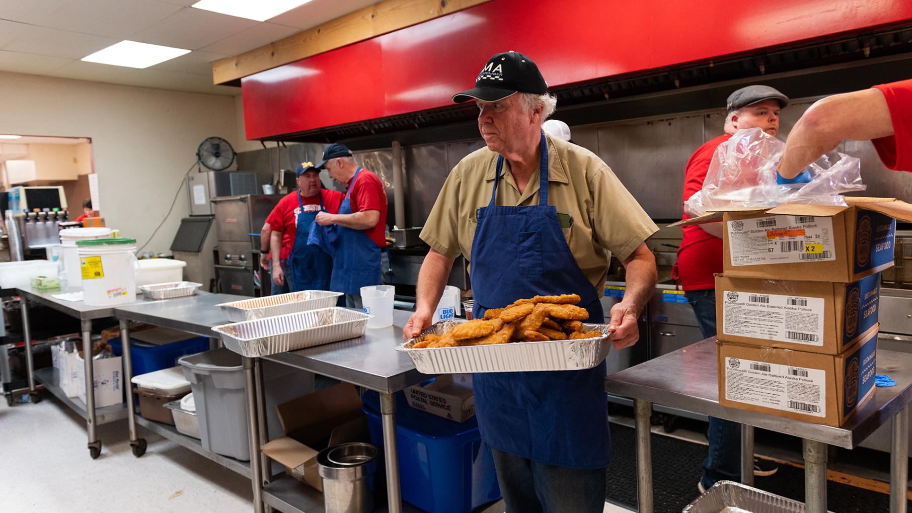 St. Christina's in Mount Greenwood has been hosting Friday fish fries for 30 years. Credit: Gonzalo Guzman for WTTW Man in kitchen carrying tray of fish fries
