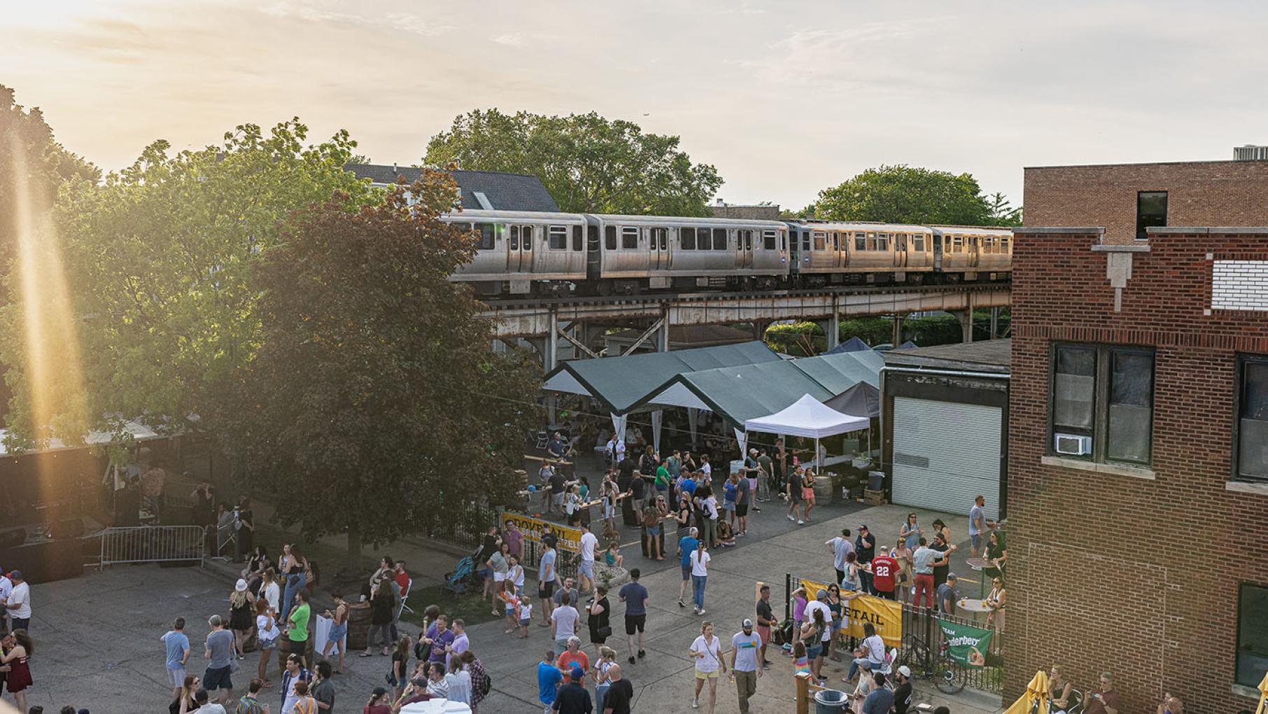 A previous Mayfestiversary in Ravenswood. Credit: Steph Byce / Mayfestiversary A Chicago Brown Line train passes by a parking lot which is filled with people and event tents