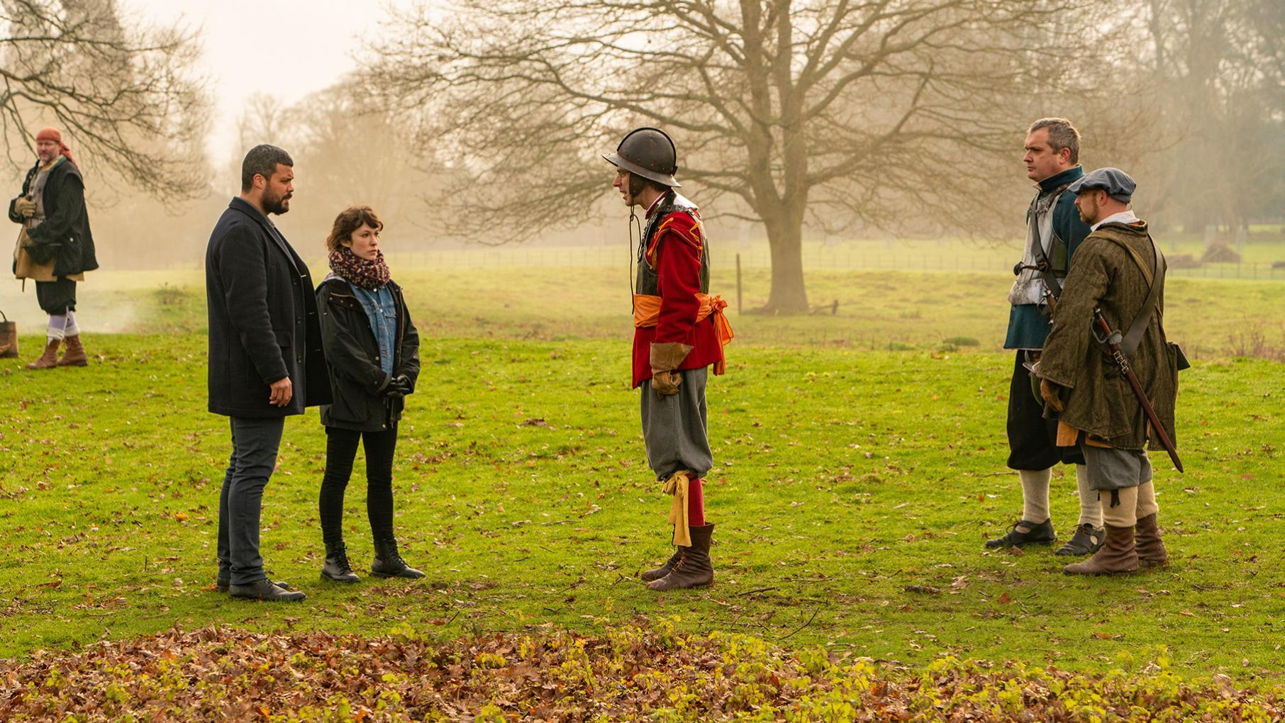 A historical reenactment goes wrong, leading Mike and Nikki to investigate Two people stand in front of a man in period military garb in a field