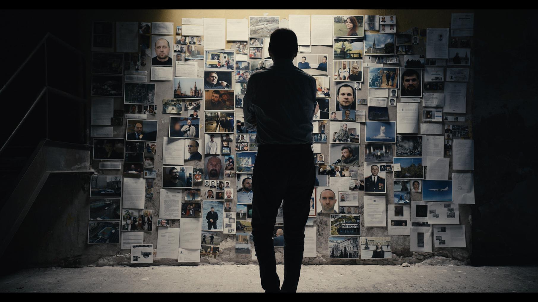 A man stands under a light before a wall of photos and articles