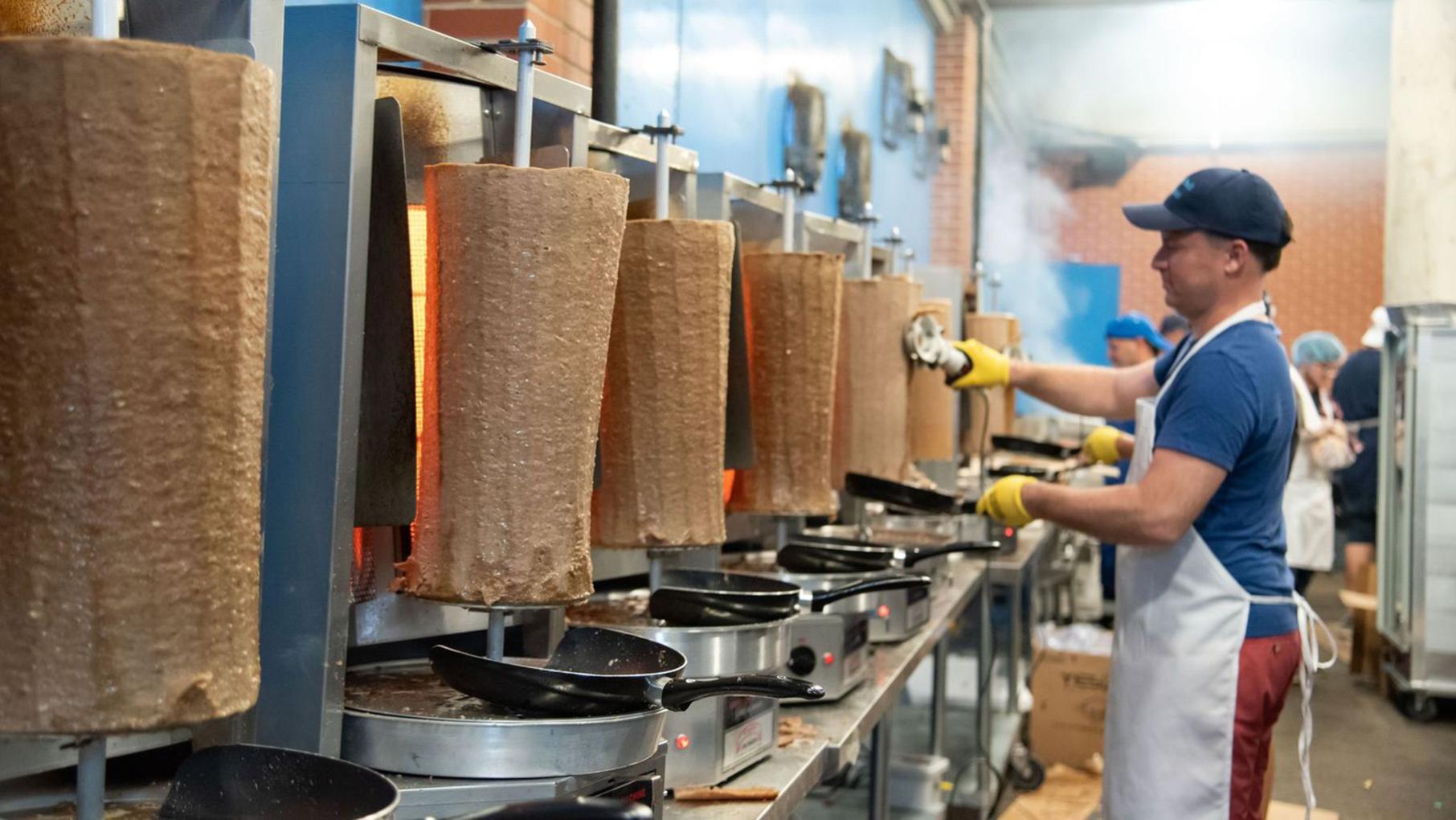 A man taking meat of revolving gyro stands