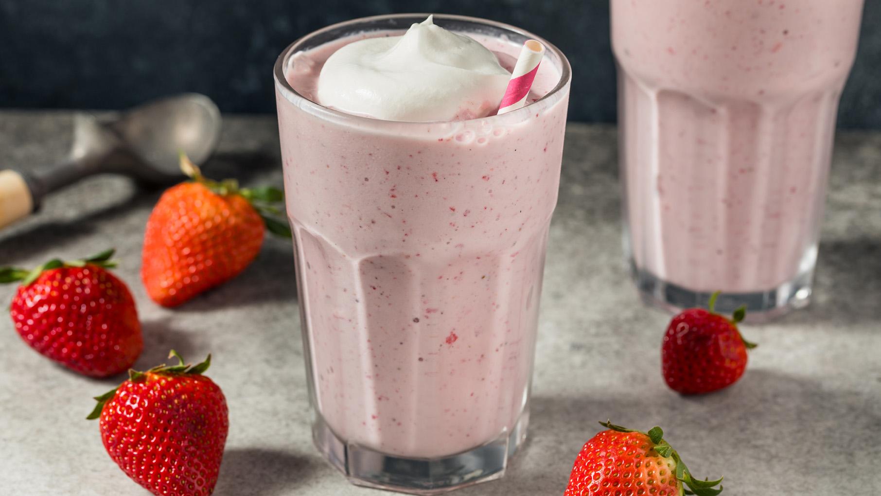 A pink milkshake topped with whipped cream and surrounded by strawberries
