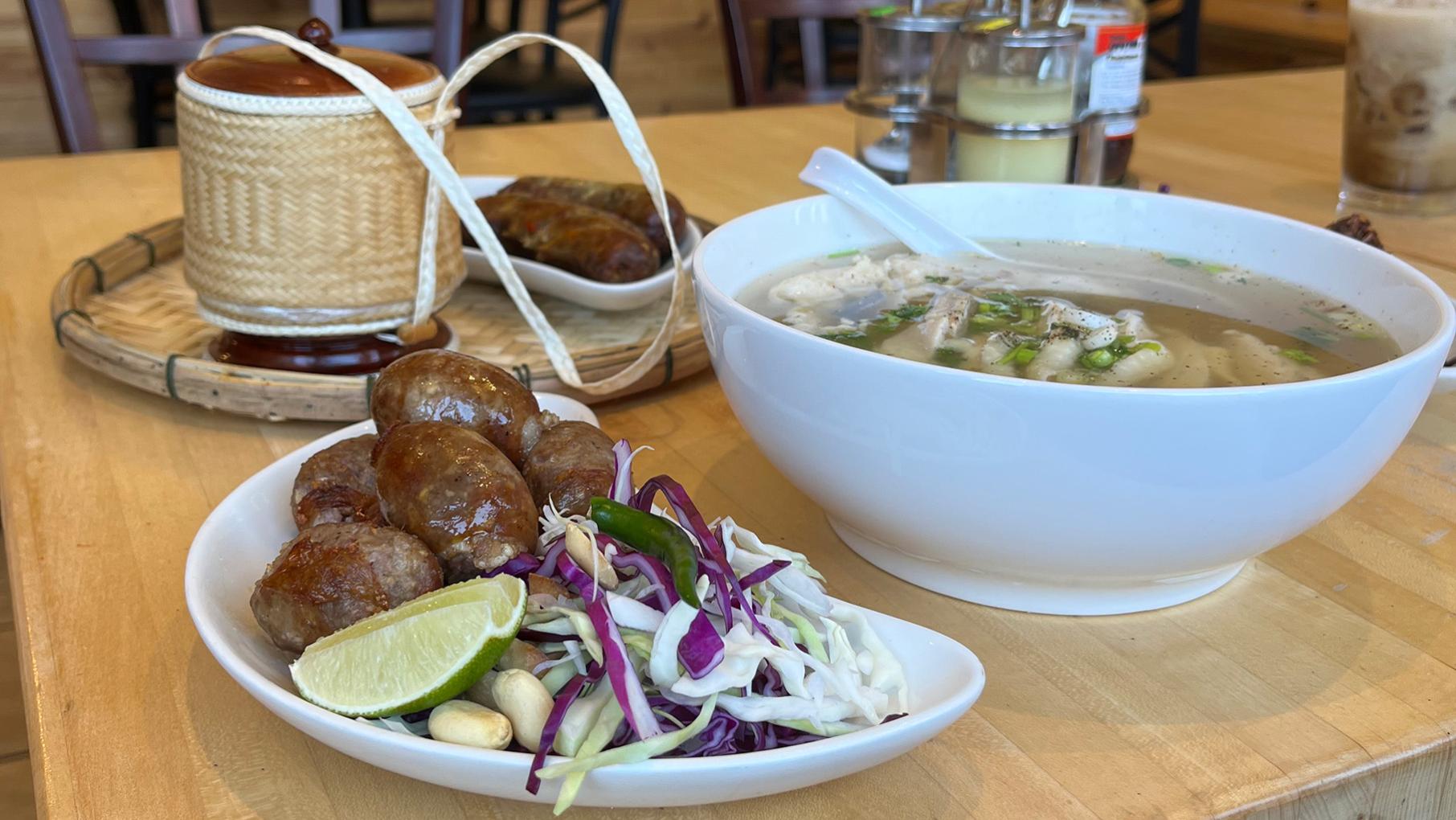 Lao Der serves Lao dishes such as Esan sausage, khao piek sien, and sai ua sausage accompanied by the essential sticky rice. Credit: Daniel Hautzinger for WTTW Several plates of Lao food, including sausage and a bowl of soup