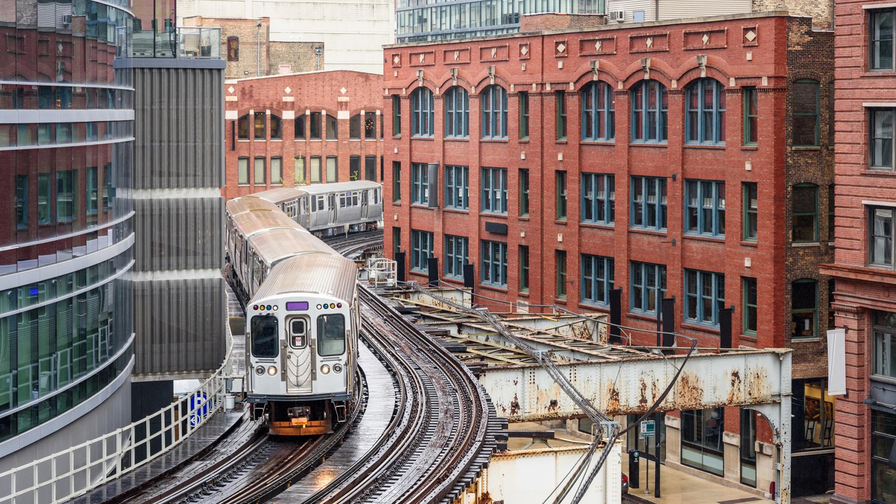 A Chicago Pink Line train winds through buildings on an elevated track downtown 
