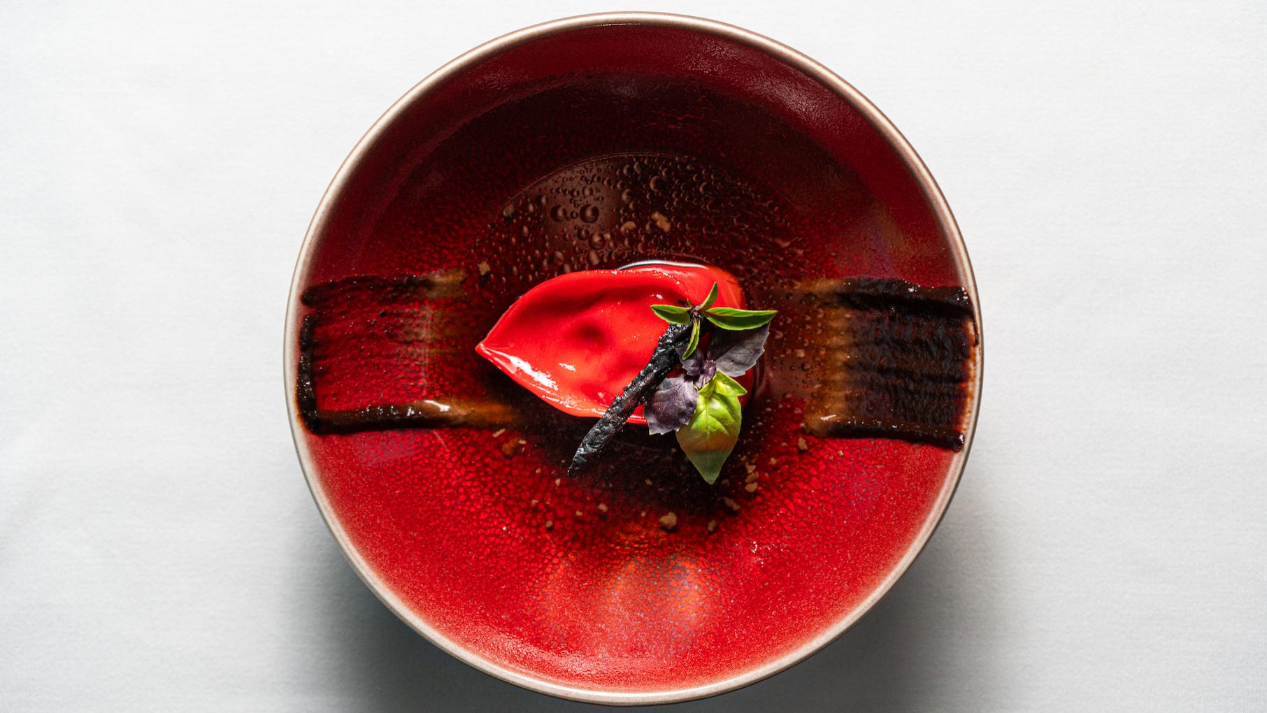 A red tortelloni topped with herbs in a red bowl against a white background