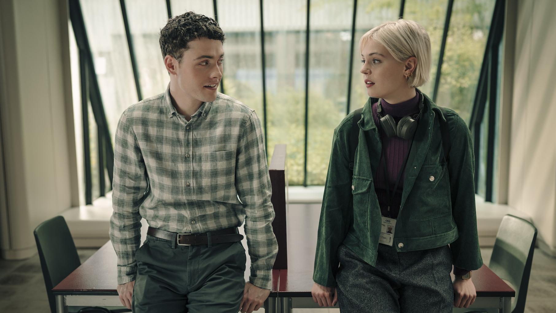 Elliot and Patience sit next to each other on a table and look at each other