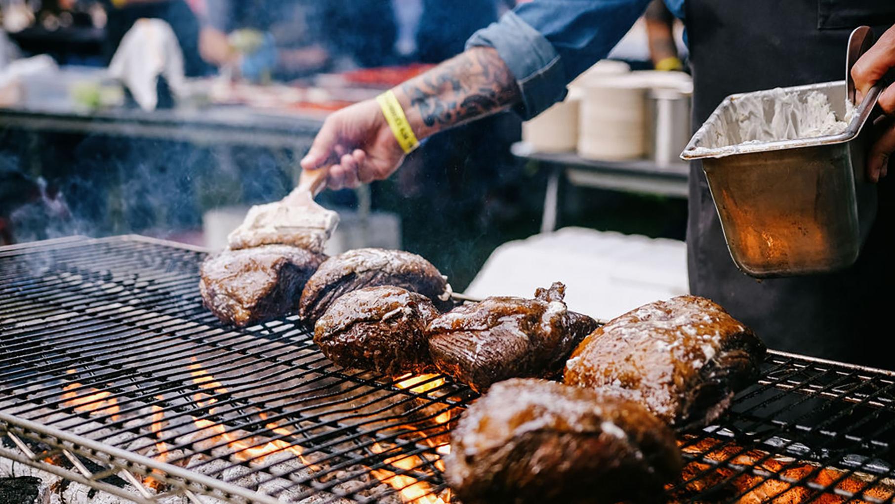 A close-up of a chef's hand brushing a cut of meat with sauce