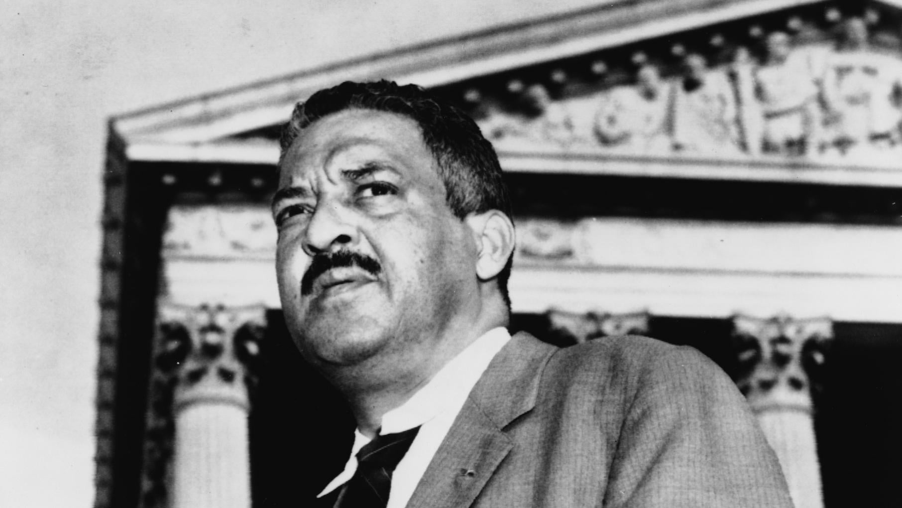 Thurgood Marshall poses in front of the Supreme Court in a black and white photo