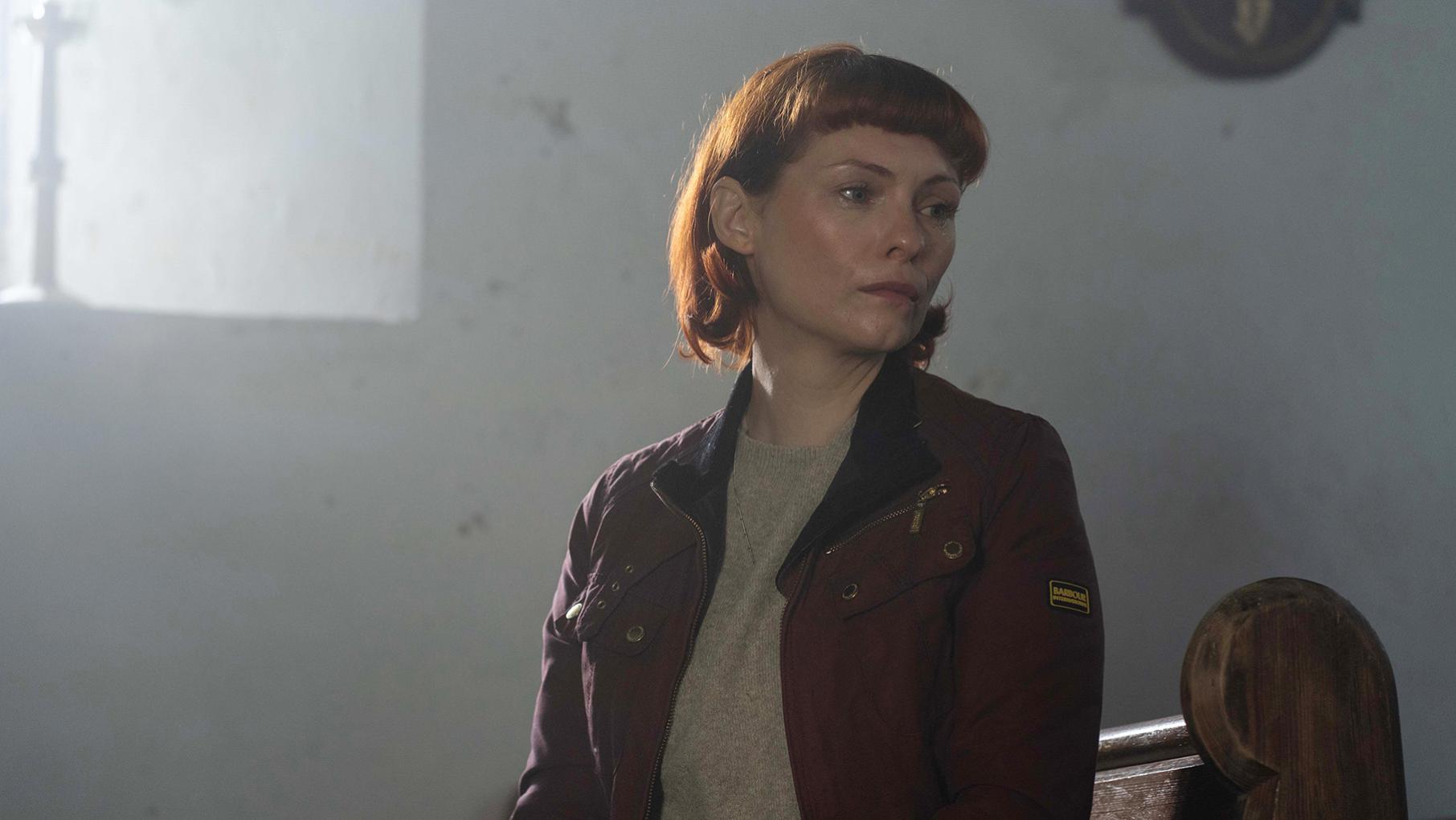 Mel looks to the side in a shadowy room by a window