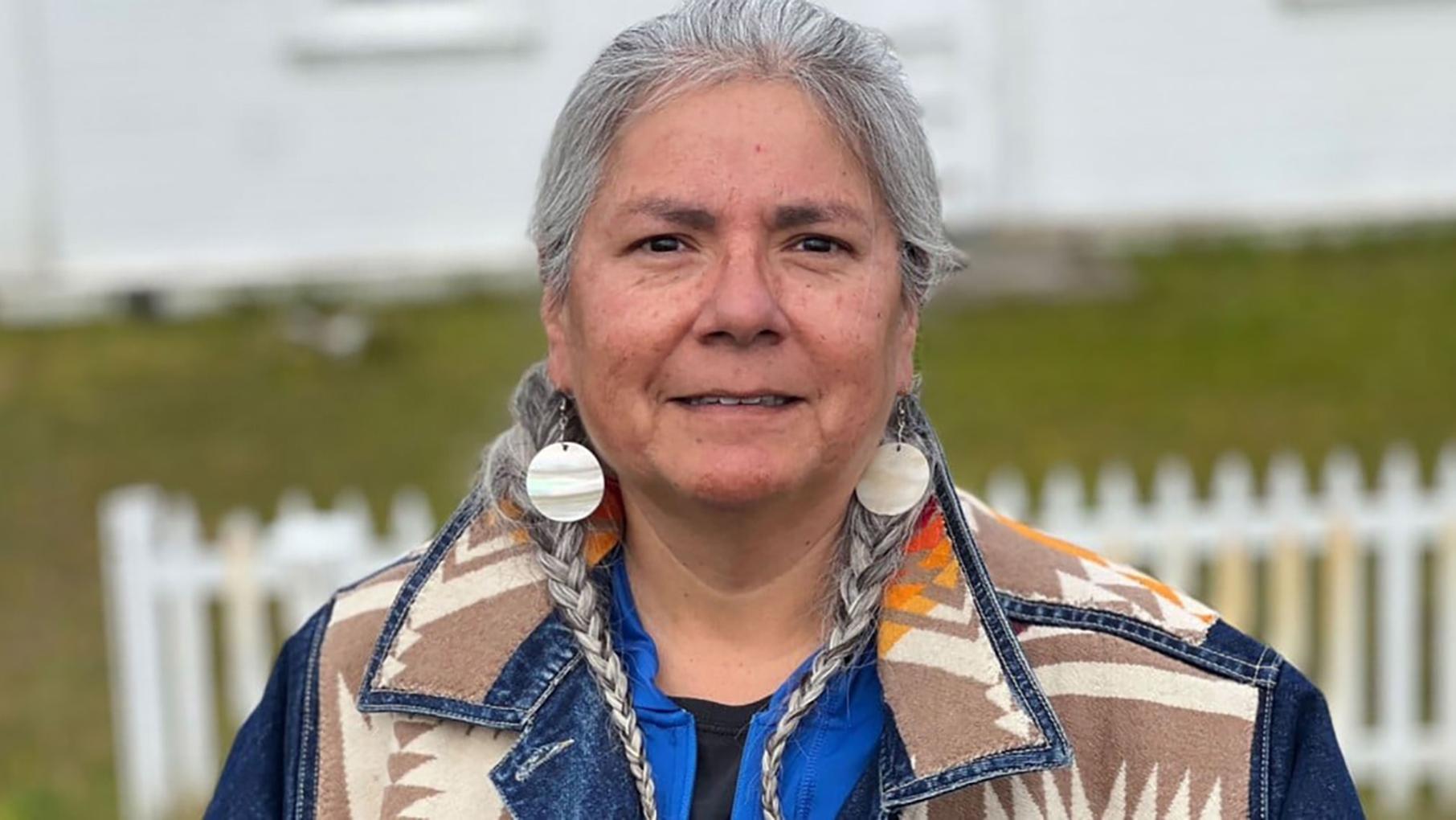 A woman with braided grey hair smiles while looking at the camera