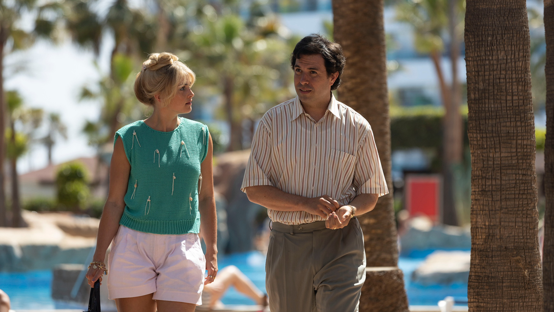 Marnie and John walk outside by palm trees and a pool
