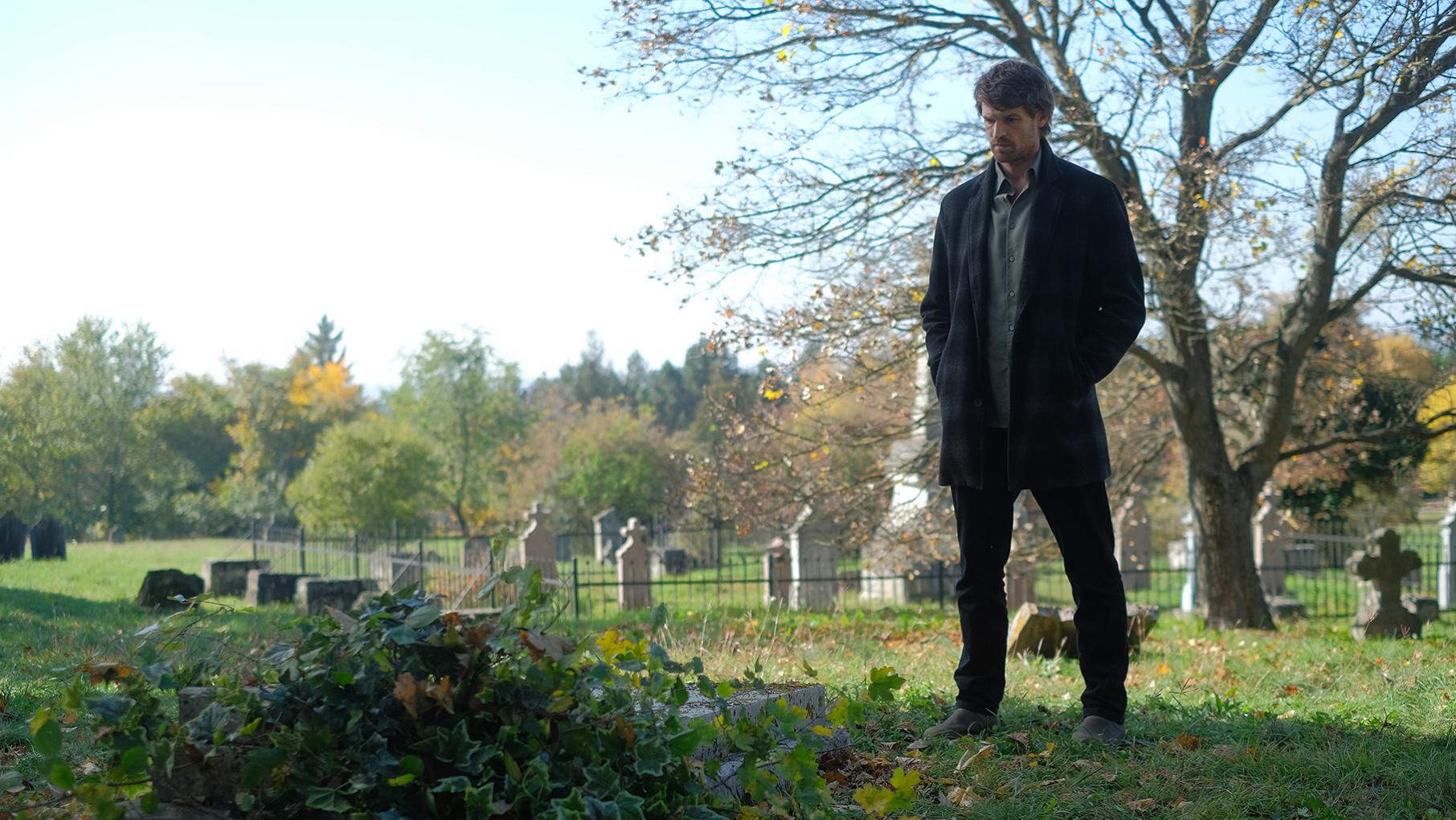 Maigret stands looking down at an overgrown grave