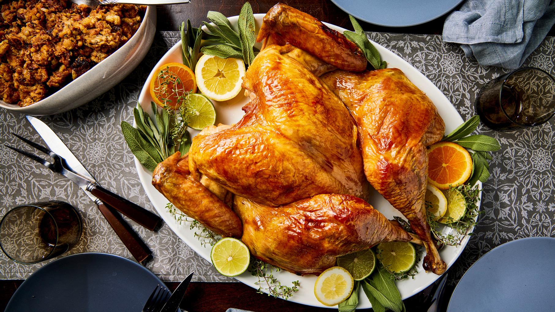 A roast turkey on a platter with lemons and herbs on a table