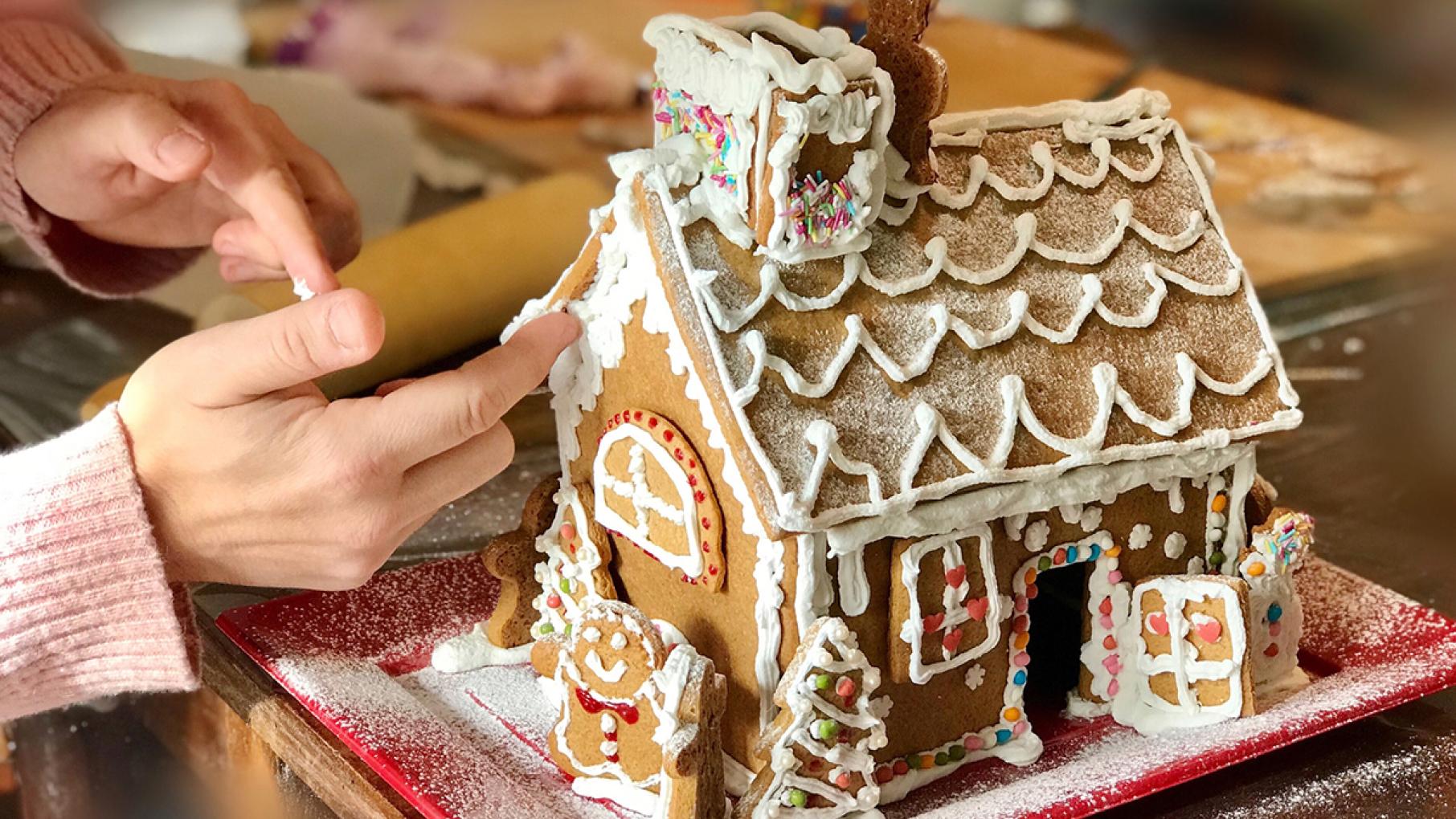 A hand reaches towards a gingerbread house