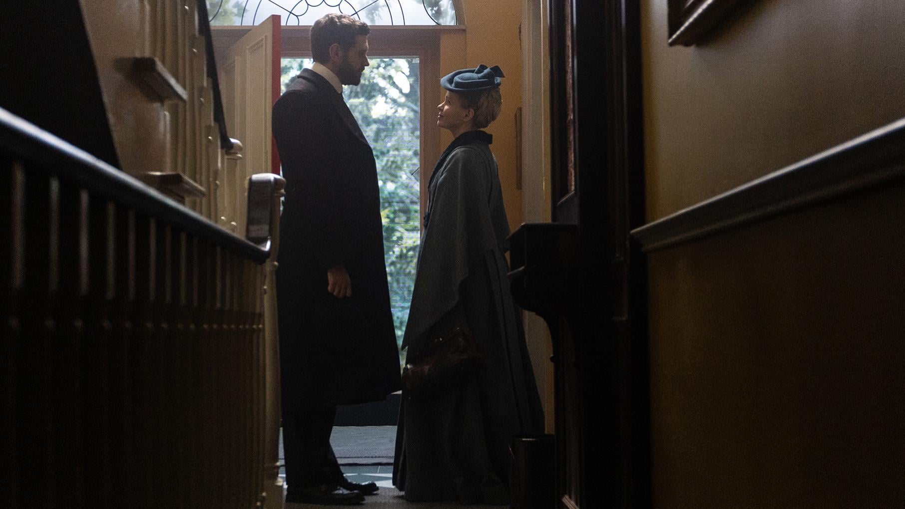 Alexander Blake and Eliza Scarlet stand facing each other in a hallway