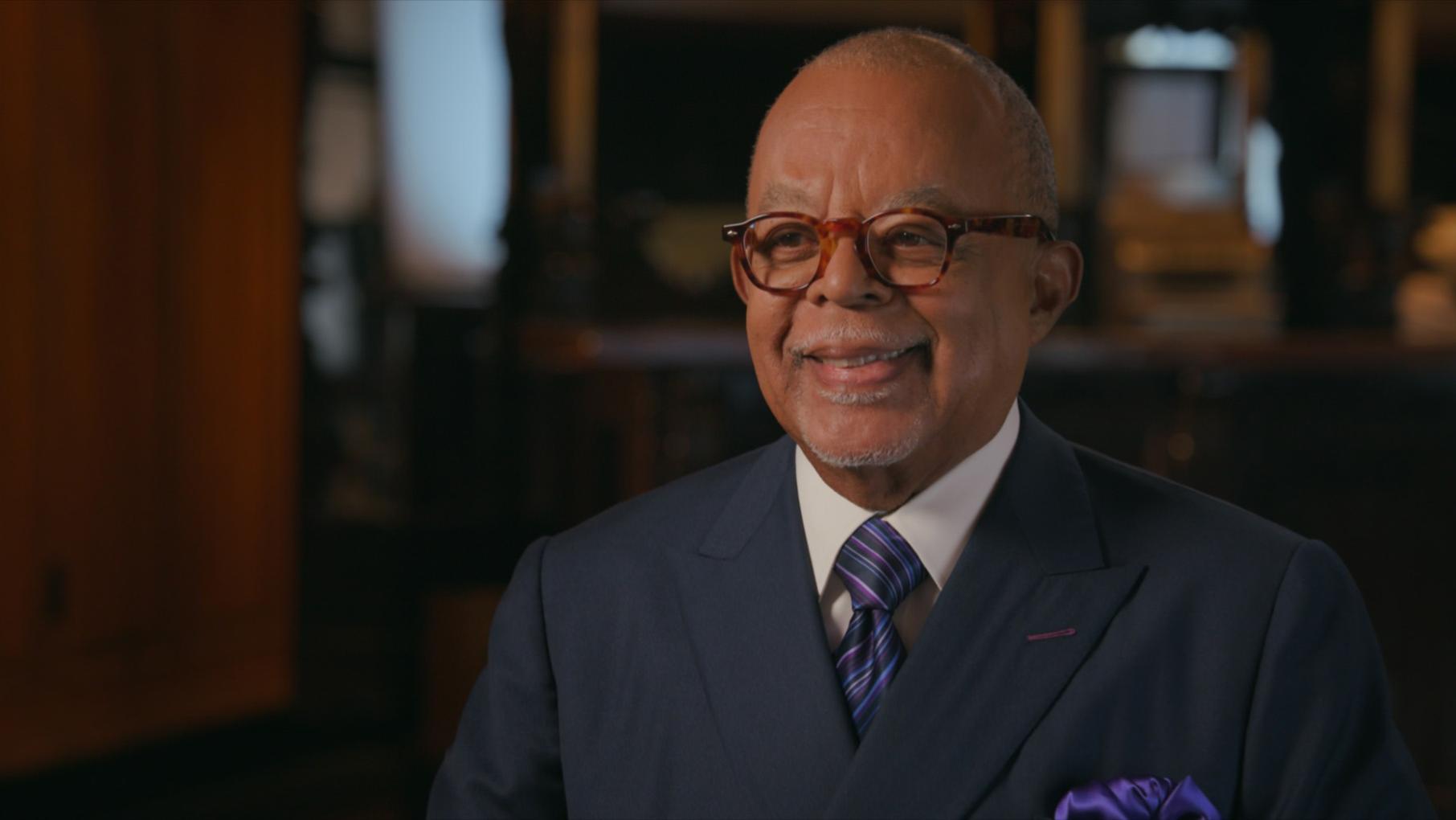 Dr. Henry Louis Gates, Jr. smiles in a suit and glasses 
